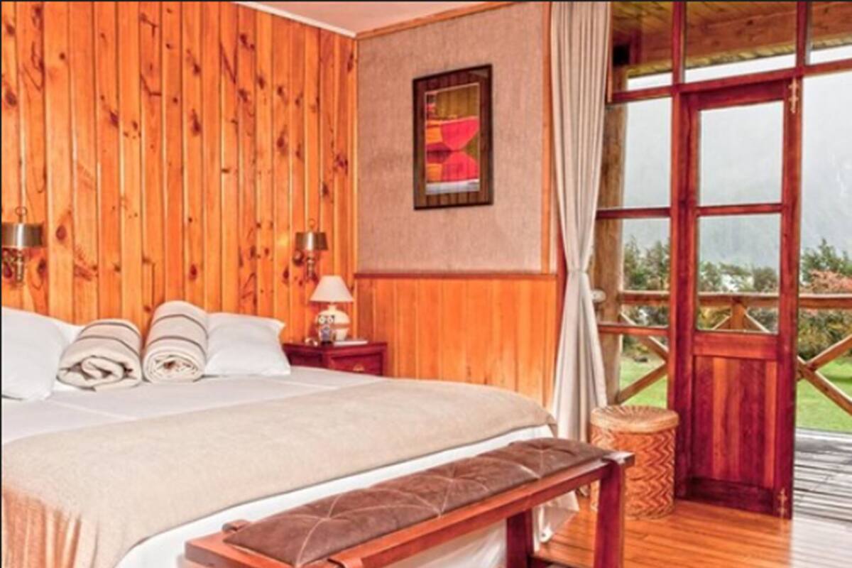 A wooden-paneled bedroom with a bed, bedside tables, a bench, and a large window.