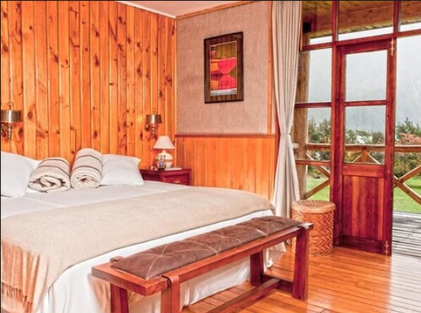 Un dormitorio con paneles de madera, una cama, mesitas de noche, un banco y un ventanal grande.