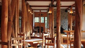 Un interior rústico de madera con techos altos y vigas a la vista, con varias mesas y sillas de madera dispuestas en un amplio comedor.