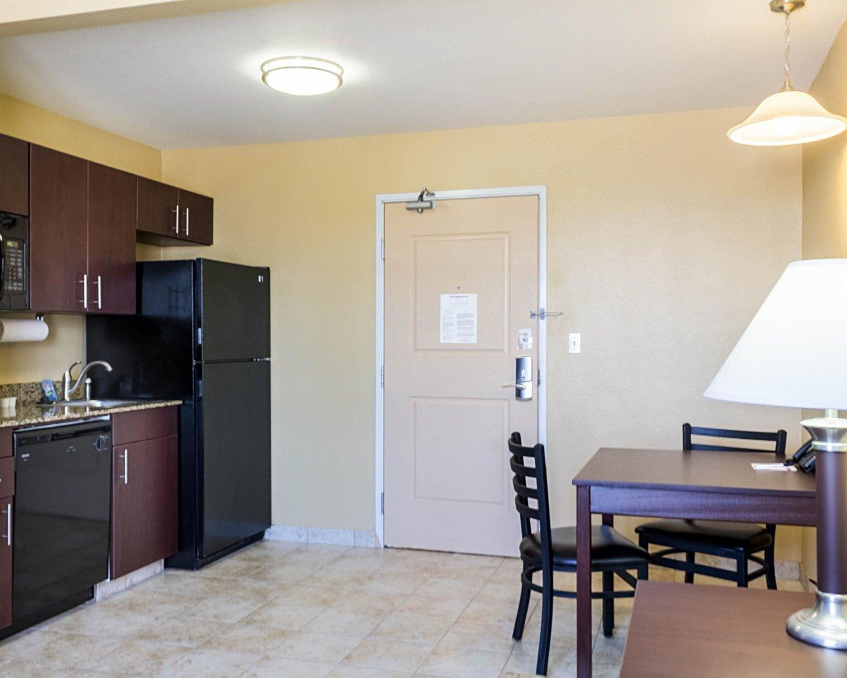 Una cocina compacta con armarios oscuros, un refrigerador negro, un lavamanos y un comedor con mesa y sillas.