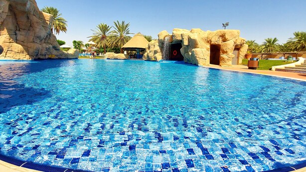 Una piscina grande y clara de color azul, con una formación rocosa y palmeras al fondo.