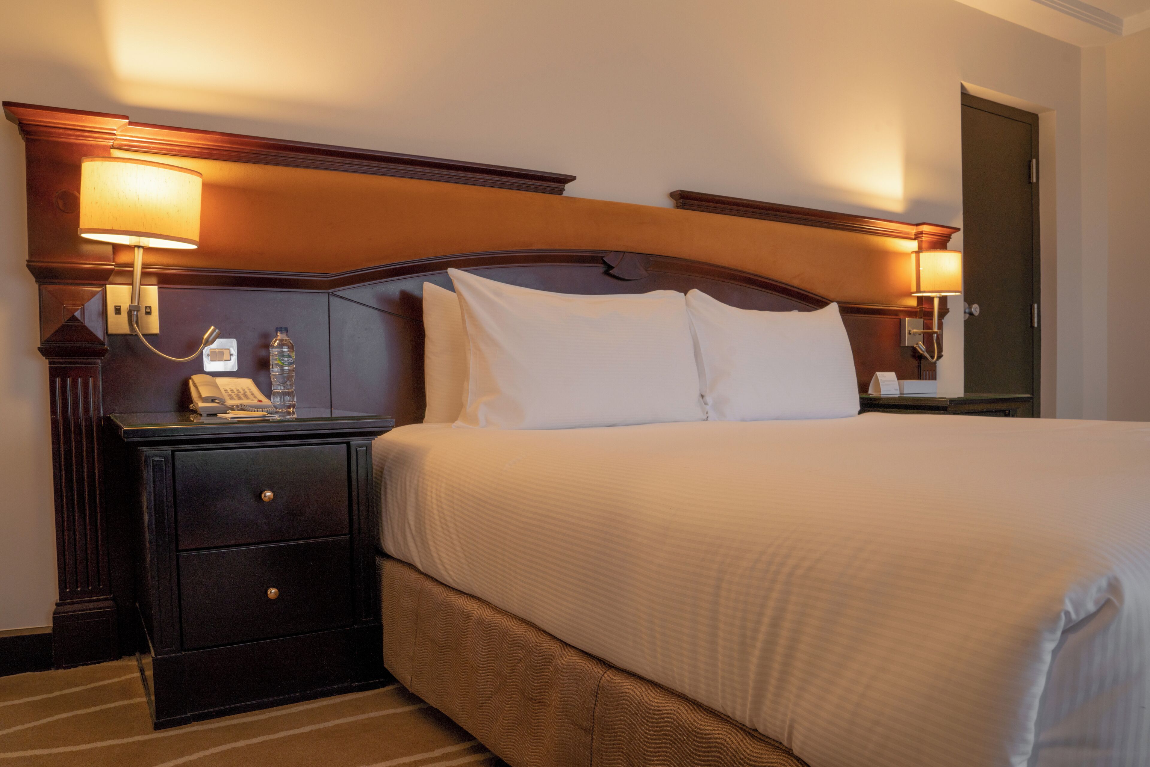 A hotel room with a large bed, two bedside tables, a nightstand, and a lamp.