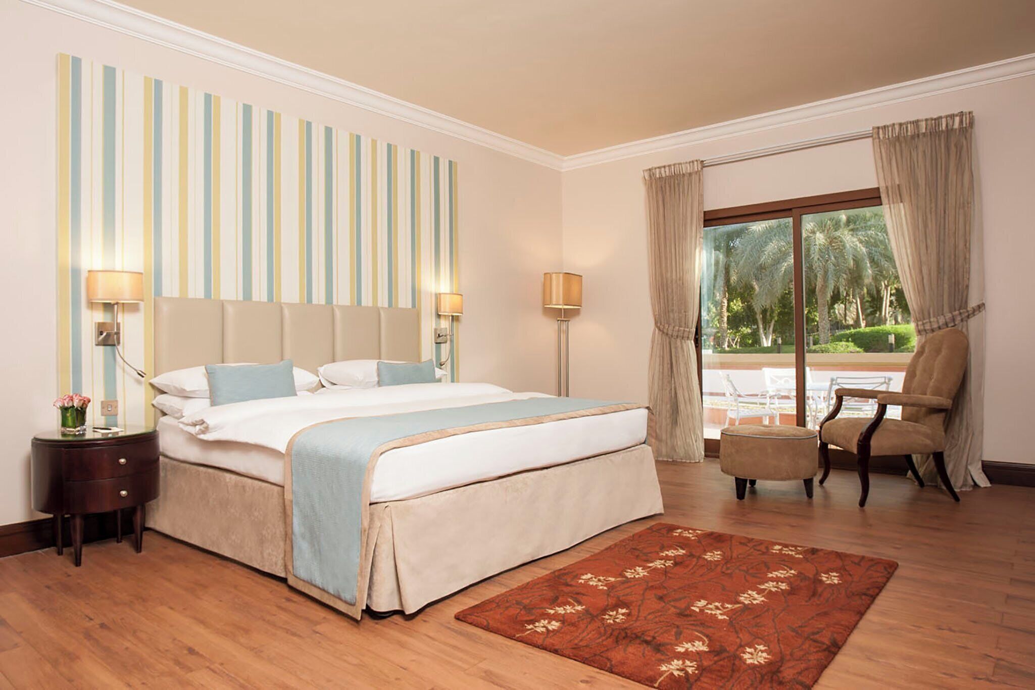 Une chambre d’hôtel avec un grand lit, une table de chevet, une chaise, une fenêtre avec des rideaux et une vue sur la verdure.