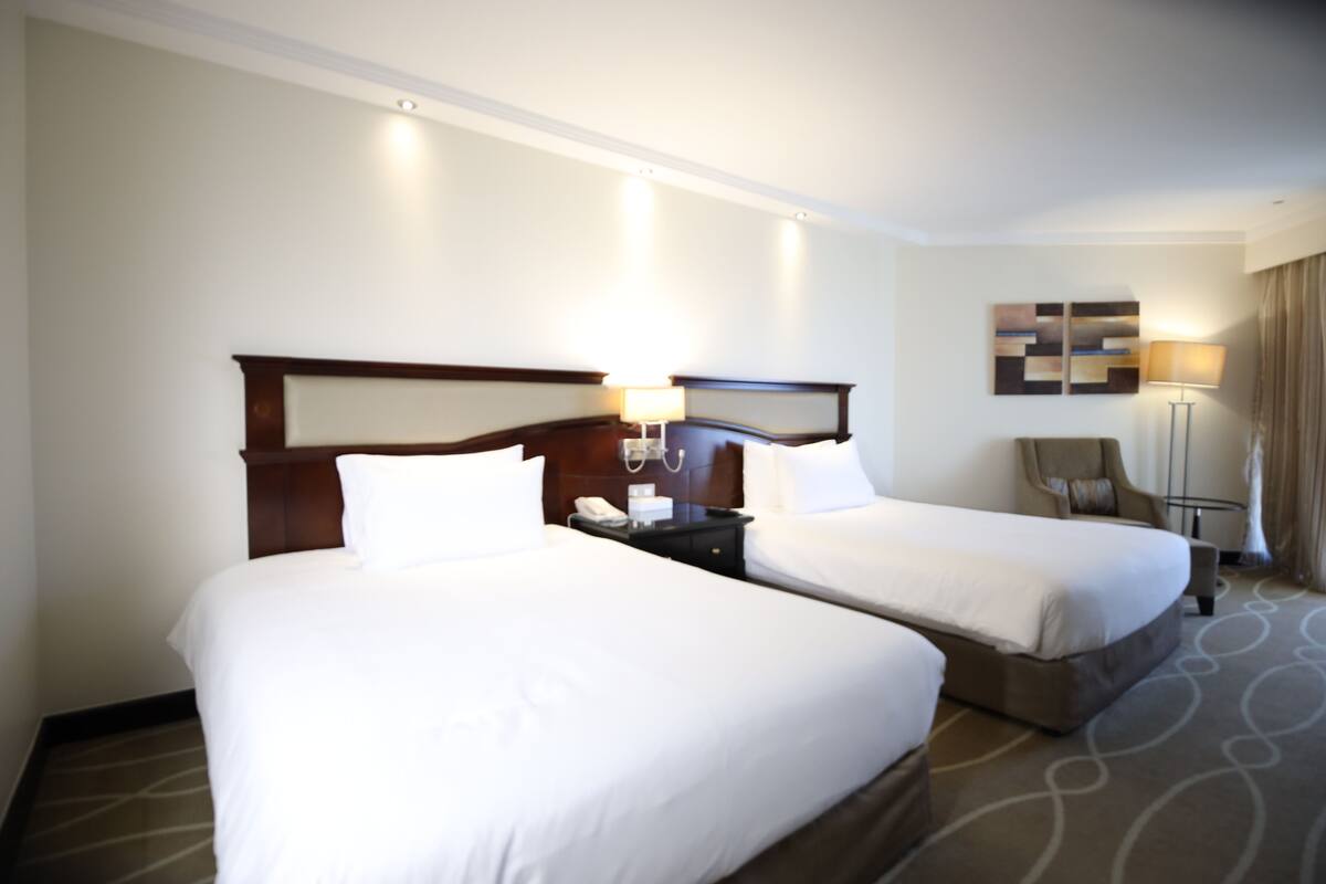 A hotel room with two beds, a nightstand with a phone, a chair, and a lamp.