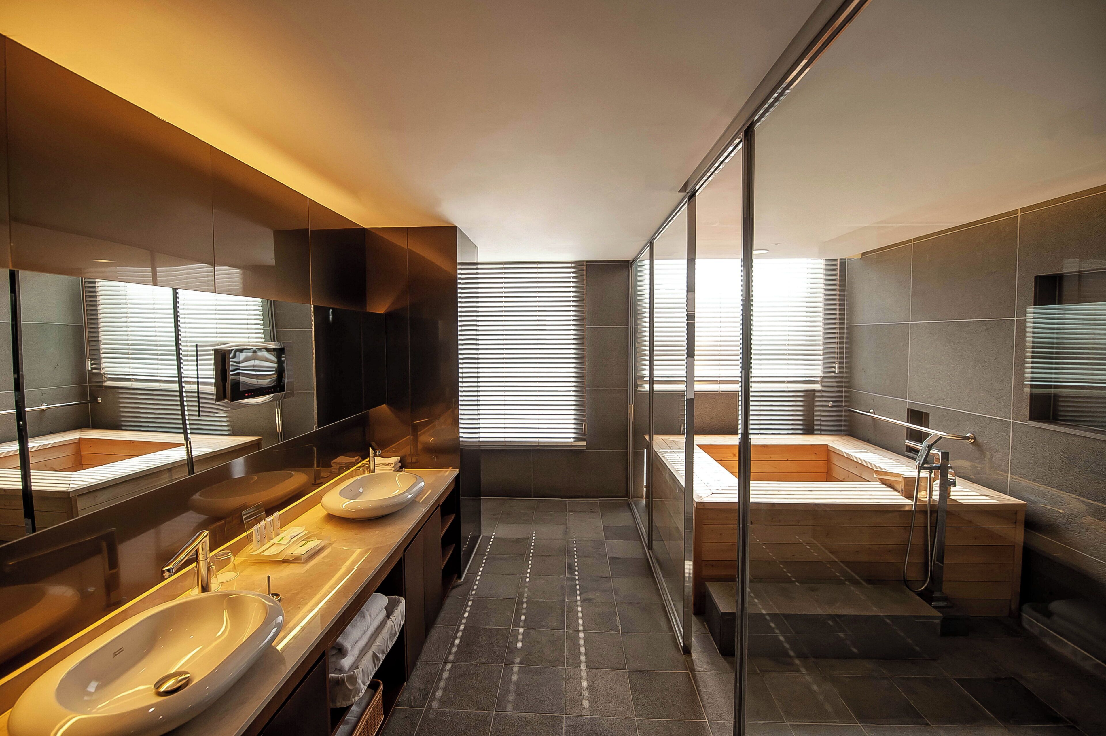 A modern bathroom with two sinks, a bathtub, and a glass-enclosed shower area.