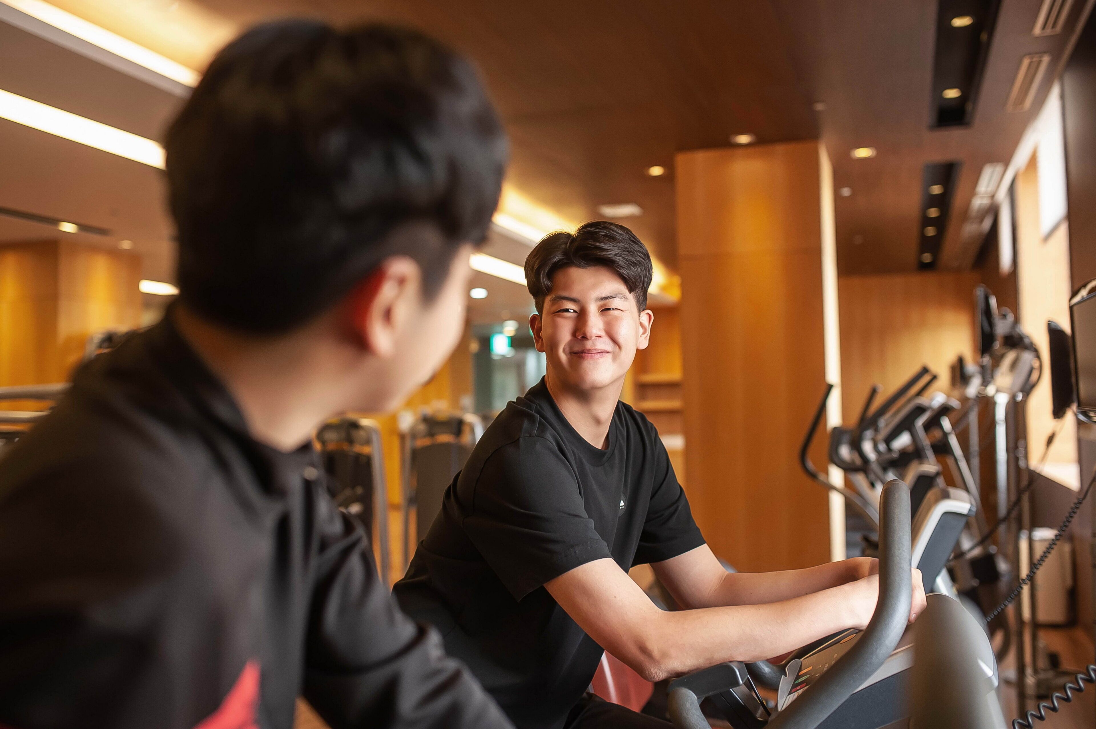 Een sportschool met trainingsapparatuur en een persoon die een hometrainer gebruikt.