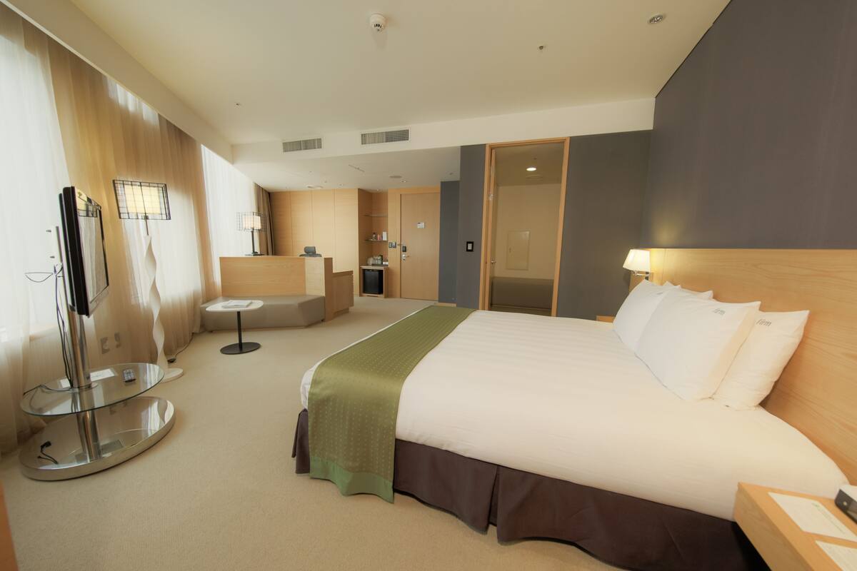 A hotel room with a large bed, a glass table, a seating area, and a separate room with a desk and chair.