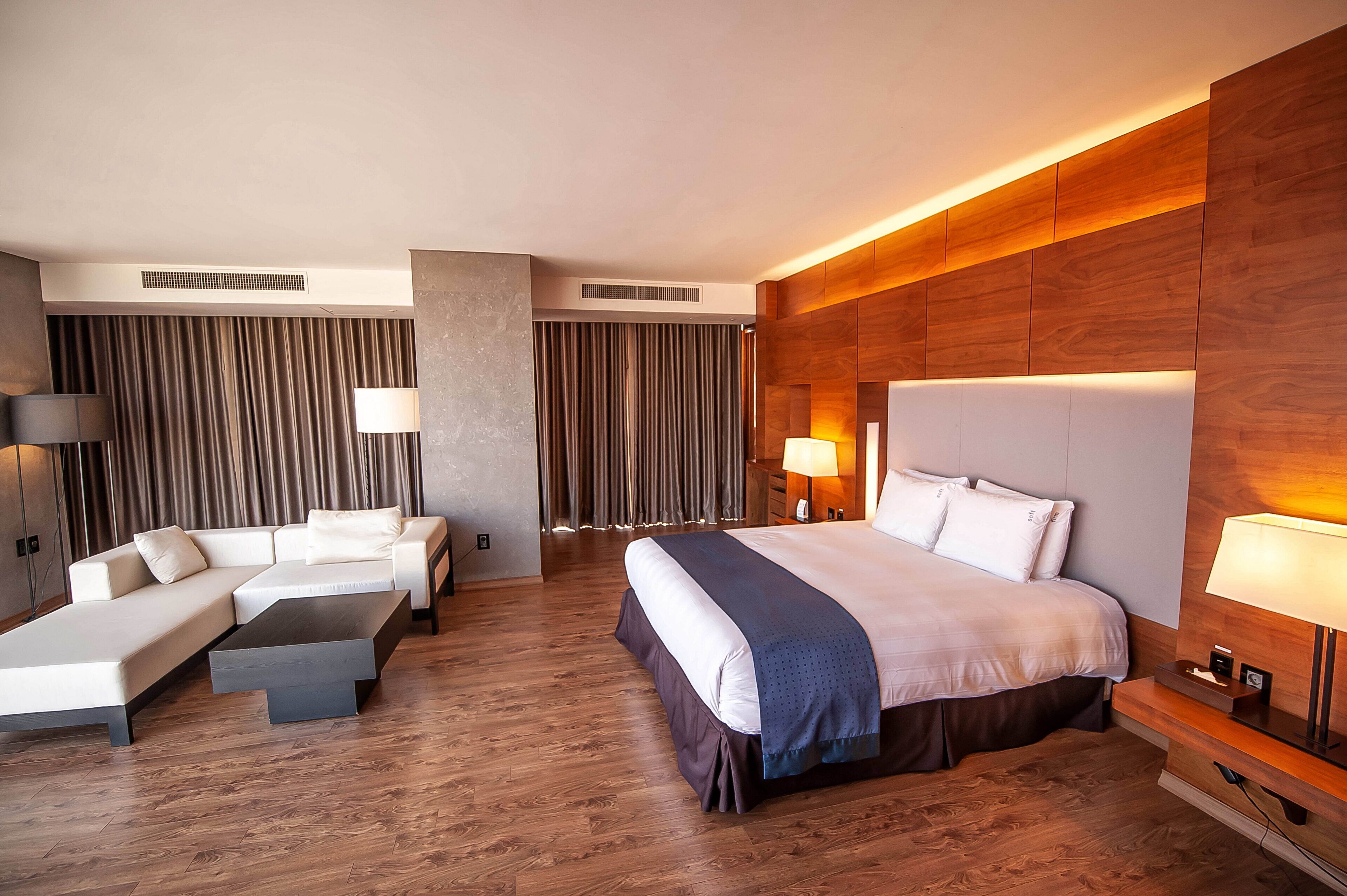 Une chambre d’hôtel moderne avec un grand lit, un canapé, une table basse et un bureau avec une lampe.
