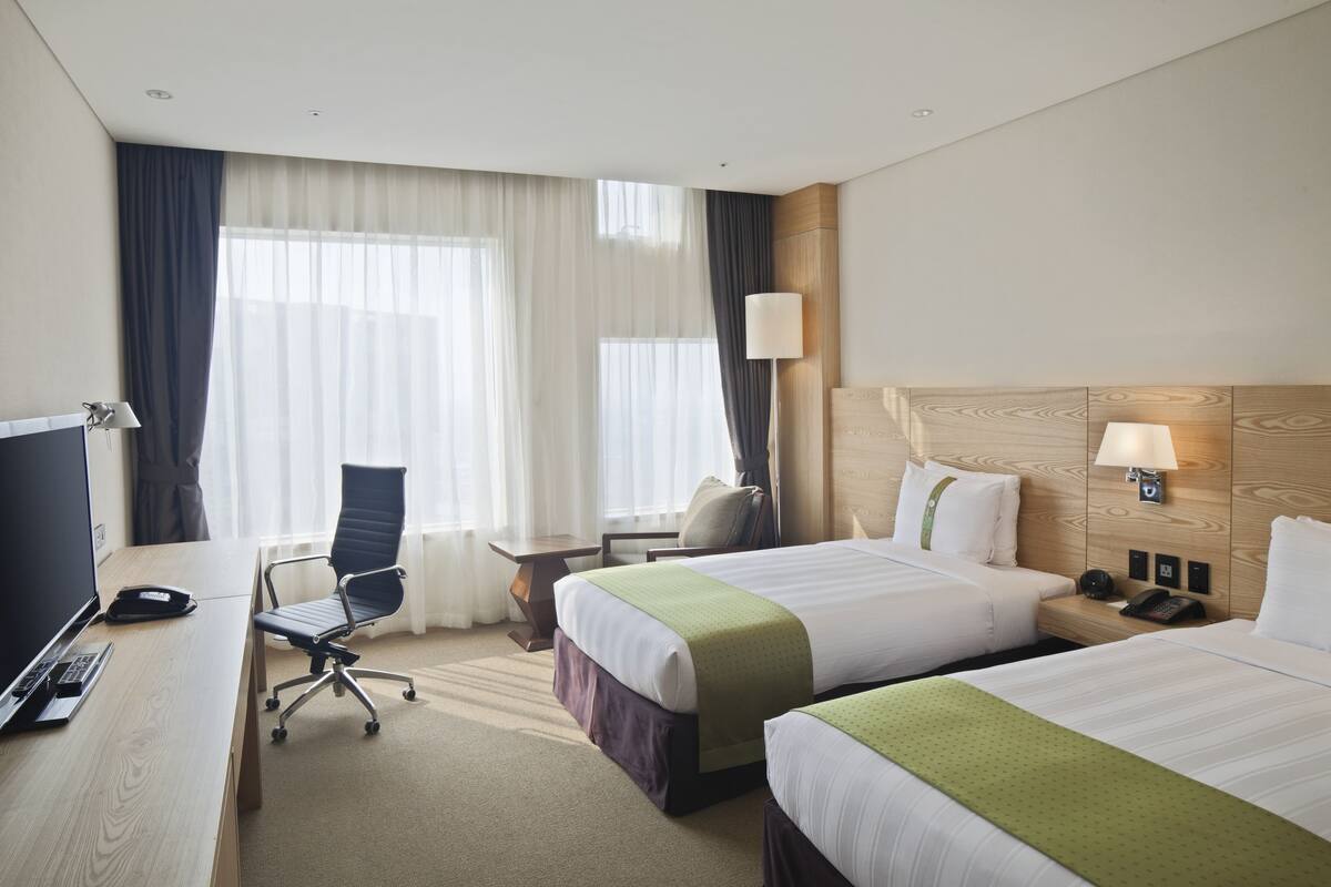A hotel room with two beds, a desk with a laptop, a chair, and a TV.