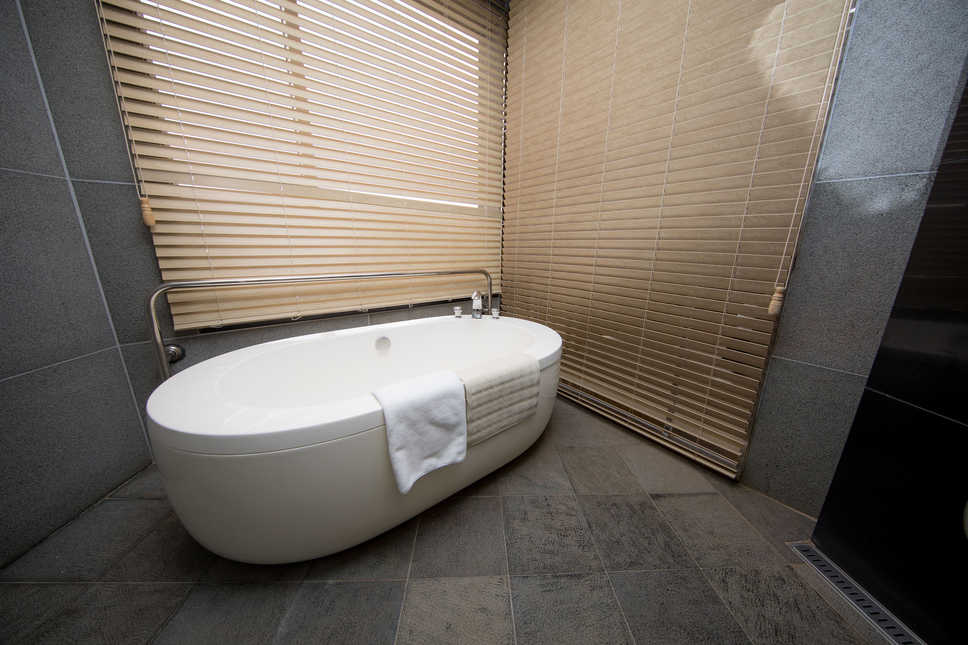 A modern bathroom with a freestanding bathtub, tiled walls, and a window with blinds.