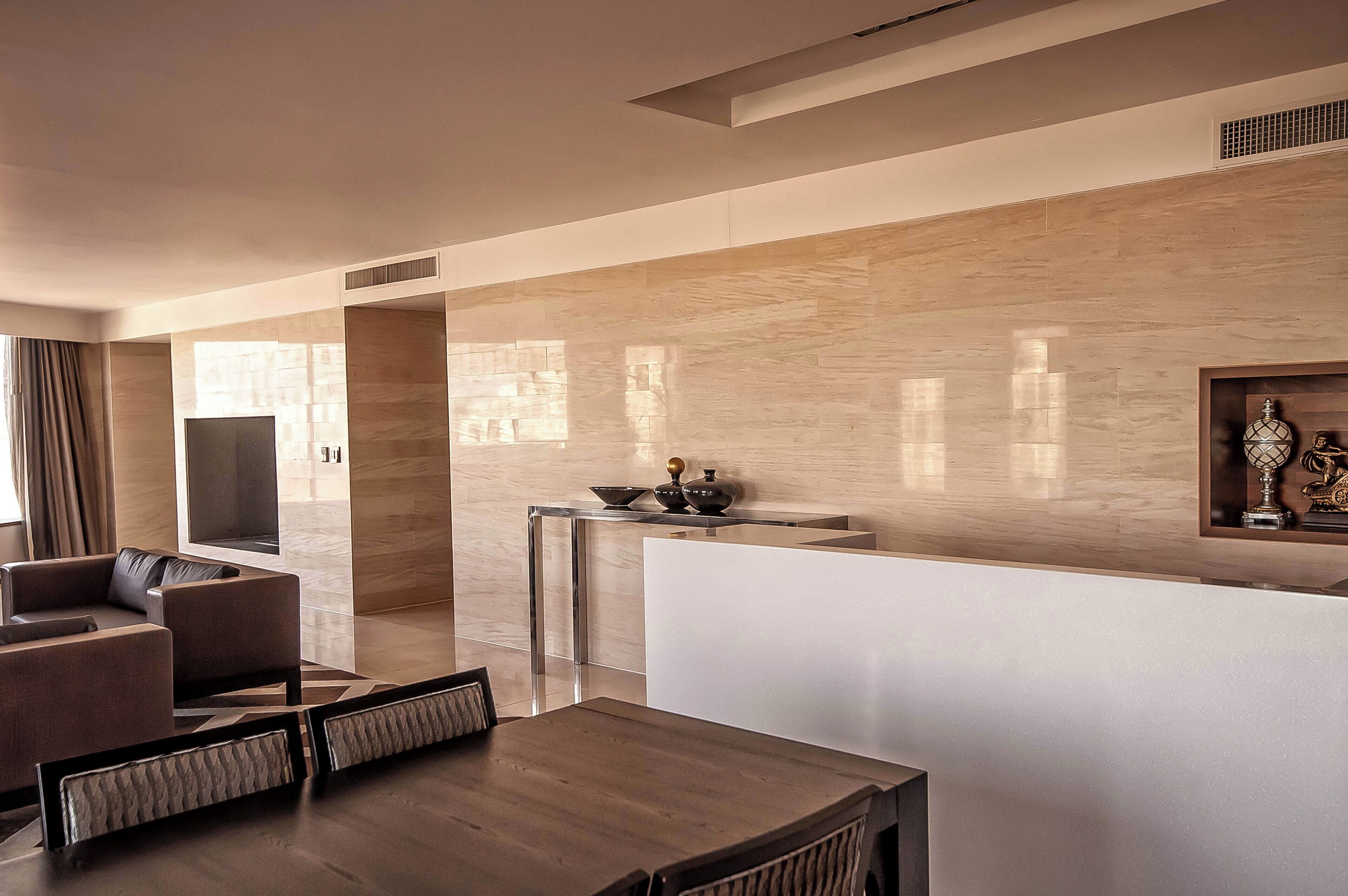 A modern hotel lobby with a wooden reception desk, a flat-screen TV, and a seating area with sofas and a dining table.