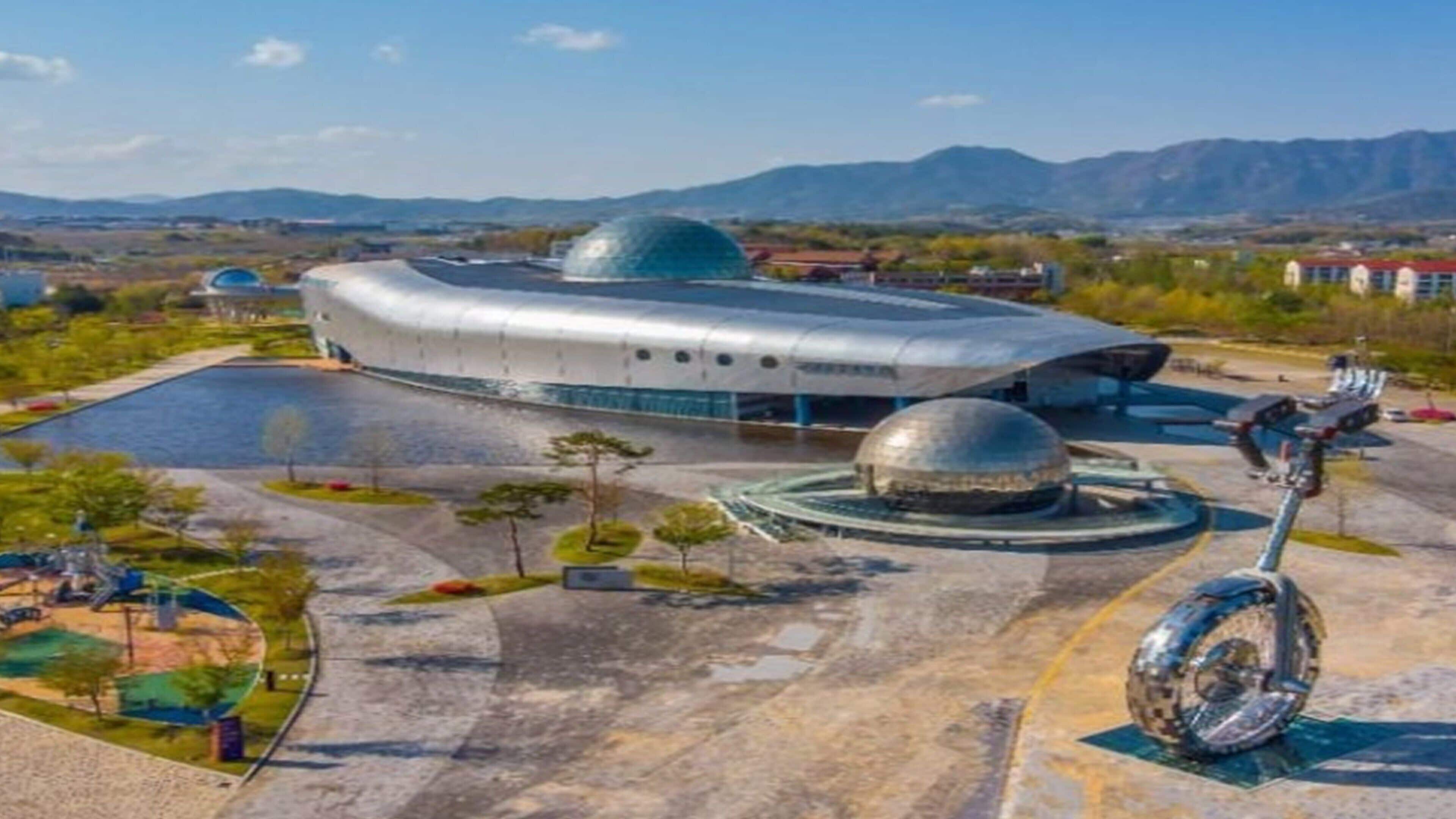 A futuristic building with a dome structure and a circular plaza with a sculpture.