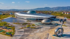 Un bâtiment futuriste doté d’une structure en forme de dôme et d’une place circulaire agrémentée d’une sculpture.