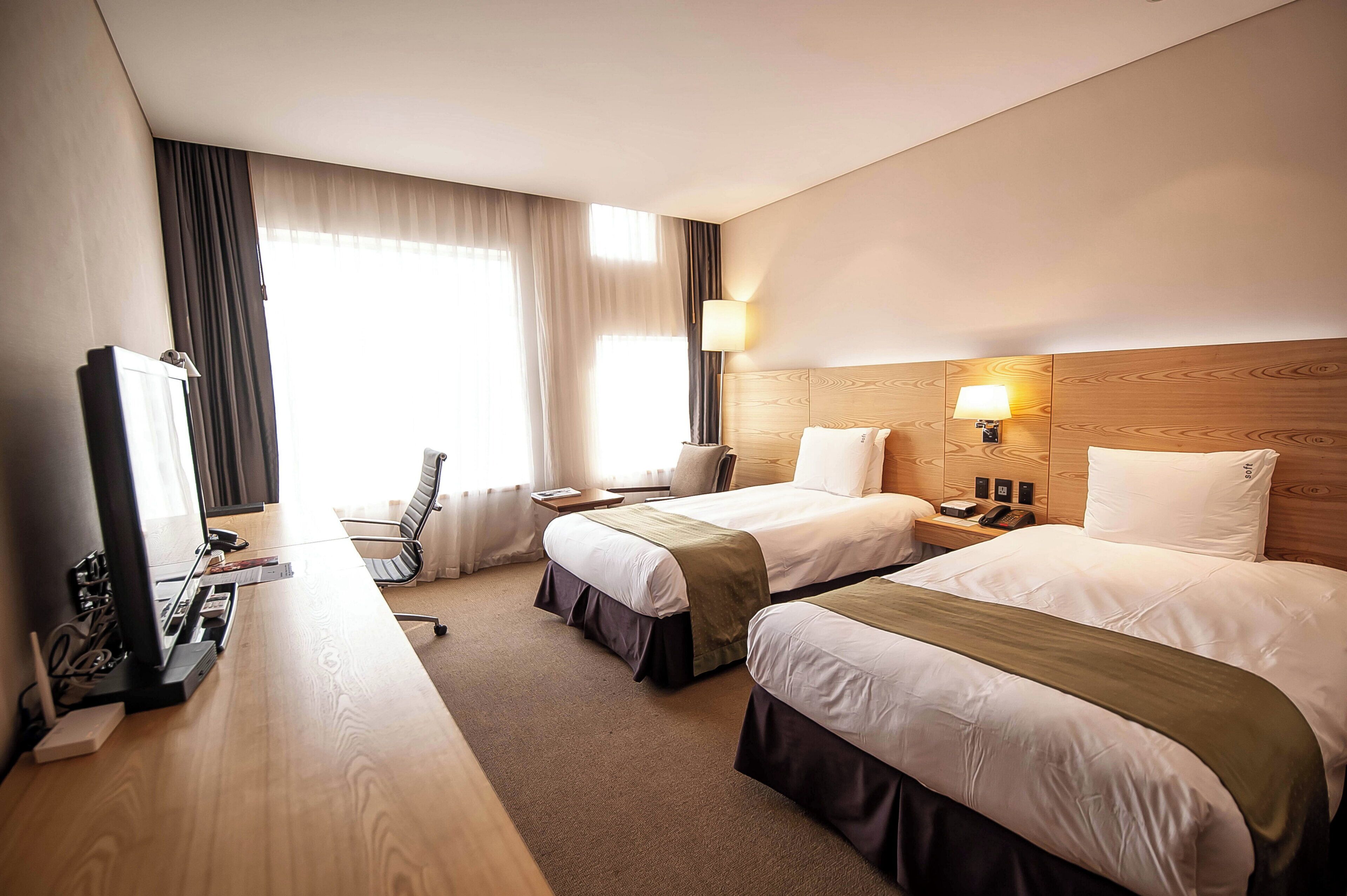 Habitación de hotel con dos camas, un escritorio, una silla, un televisor y una ventana con cortinas.