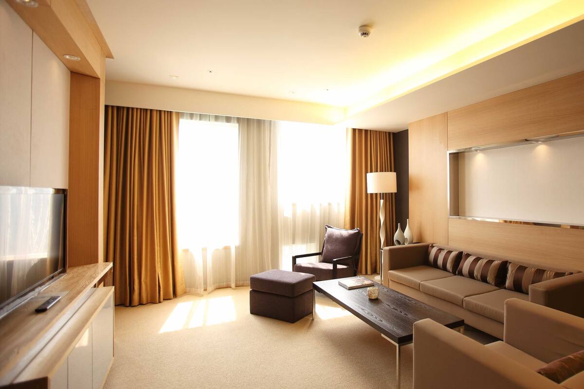 A modern hotel room with a flat-screen TV, a sofa, a coffee table, and a desk.