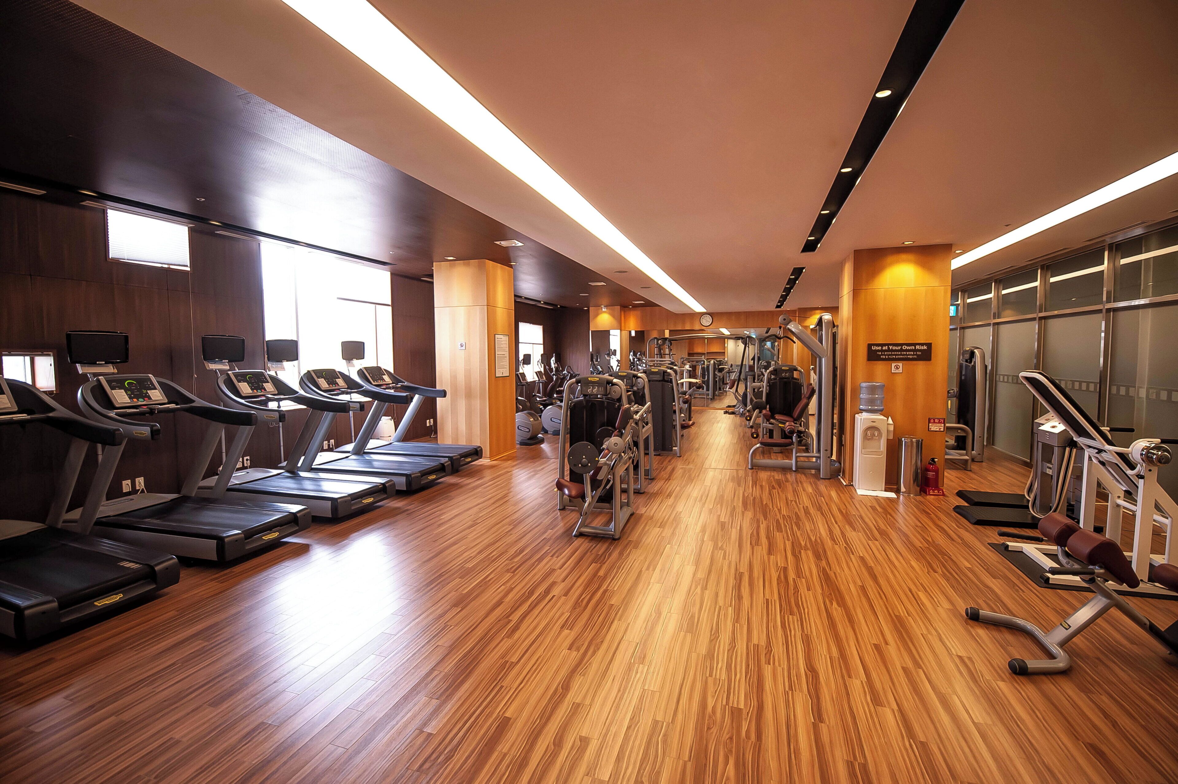 A gym with treadmills, weight machines, and a wooden floor.