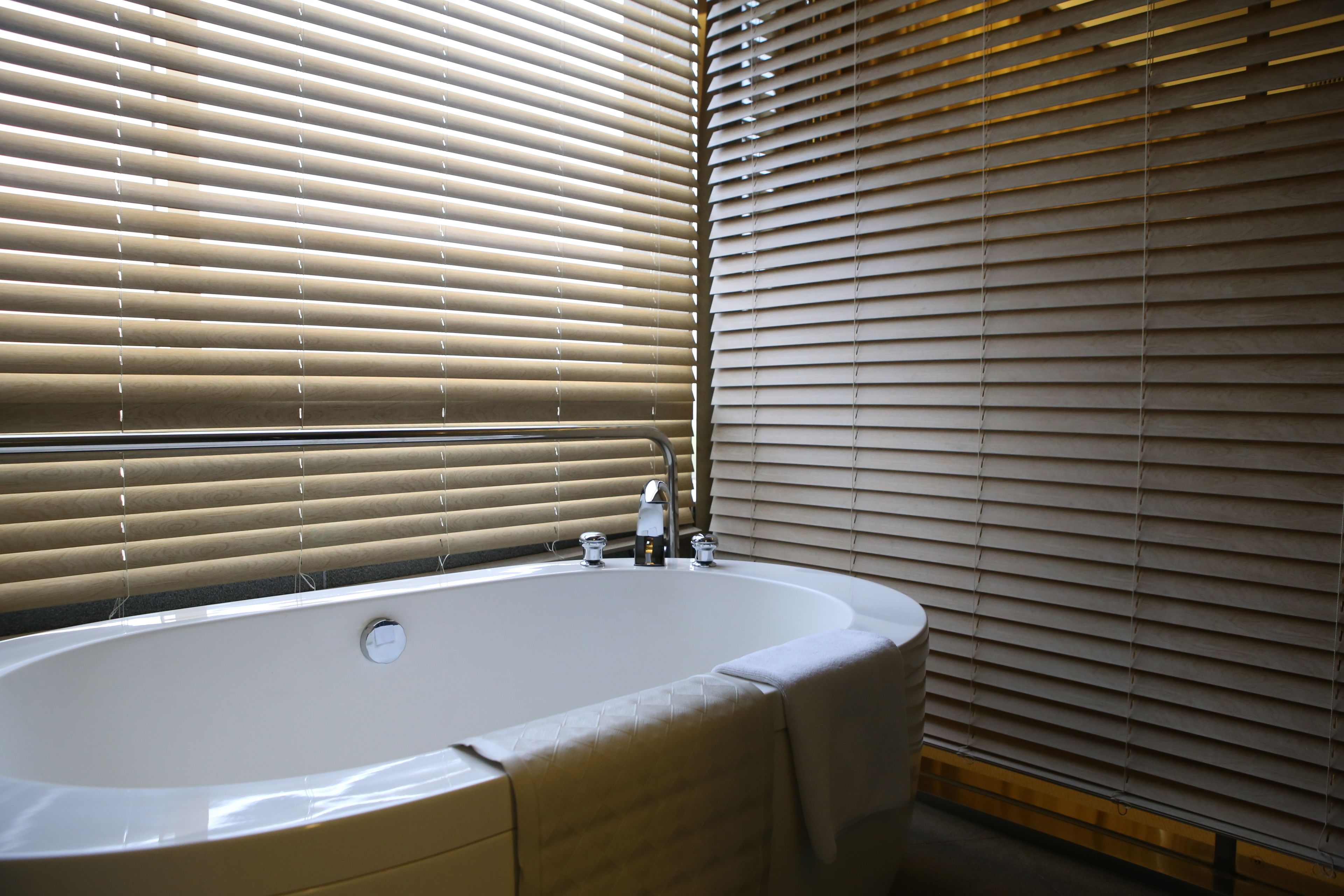 Une salle de bain avec une baignoire, un lavabo et une fenêtre avec des stores.