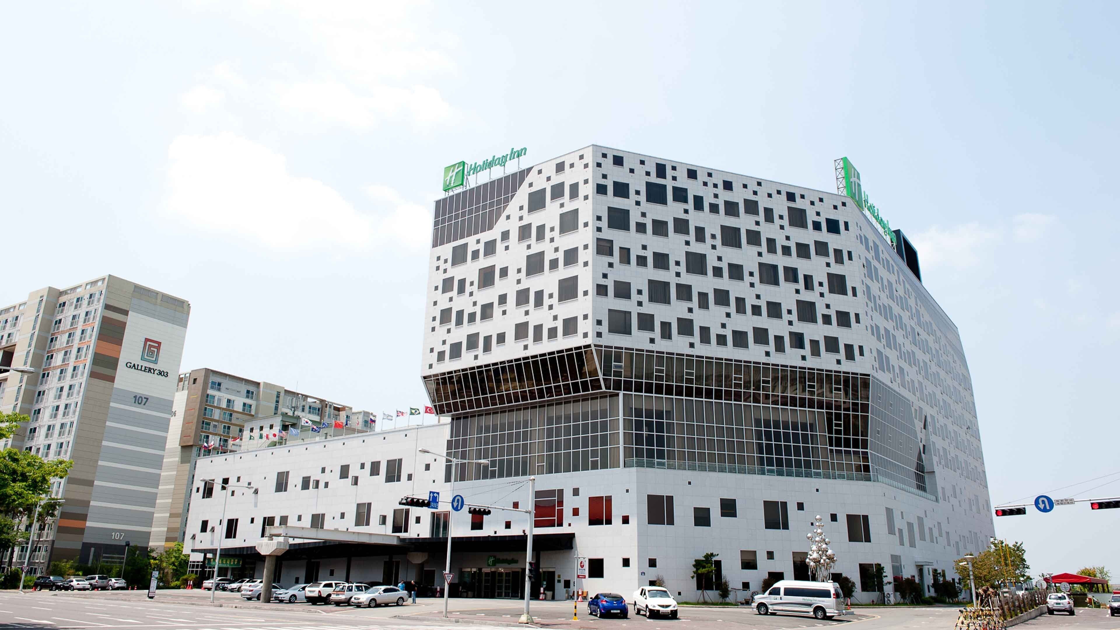 Un hôtel moderne à la façade géométrique originale, avec de nombreux étages et une enseigne Holiday Inn bien visible.