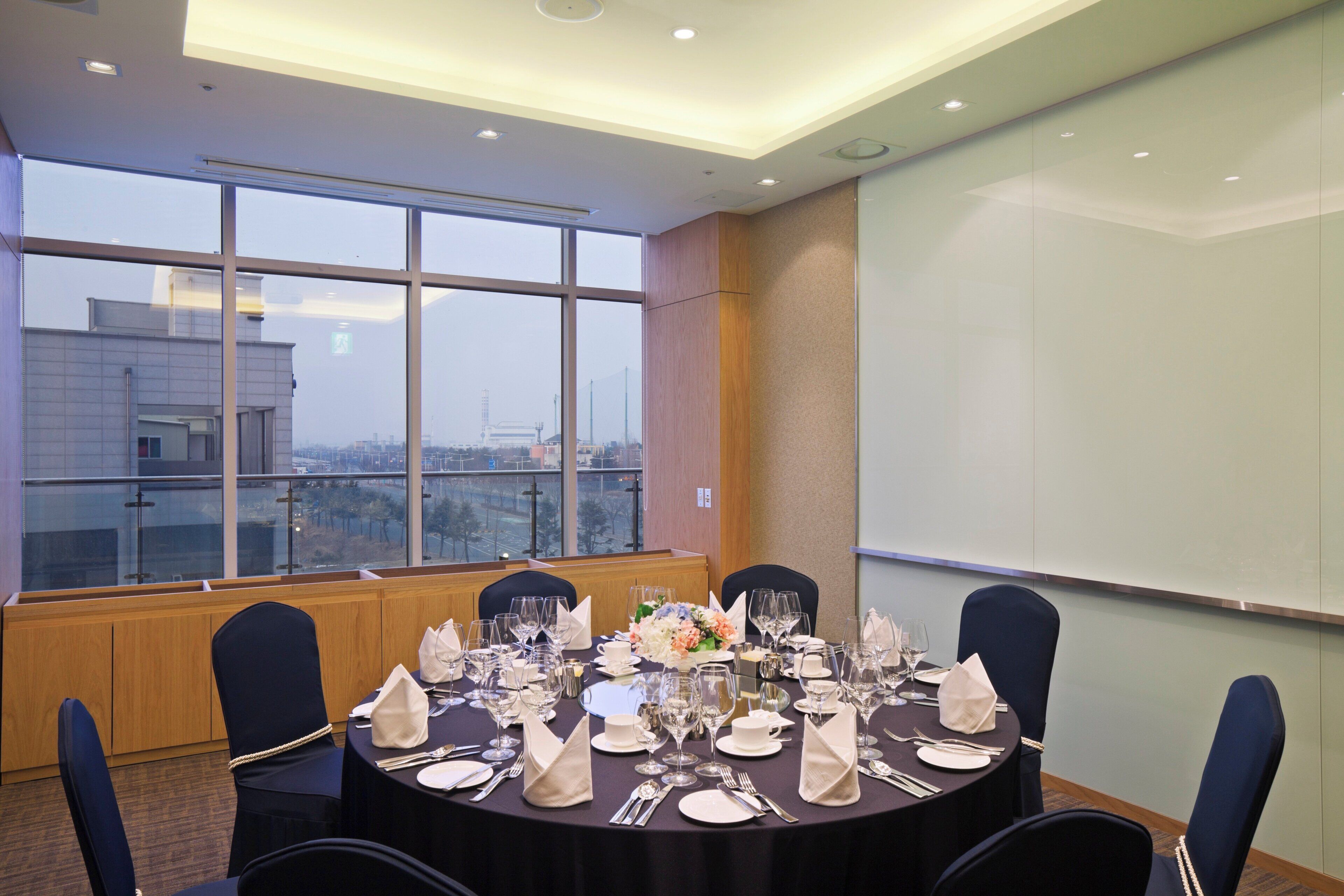 A conference room with a large table set for a meeting, large windows with a city view, and a whiteboard on the wall.