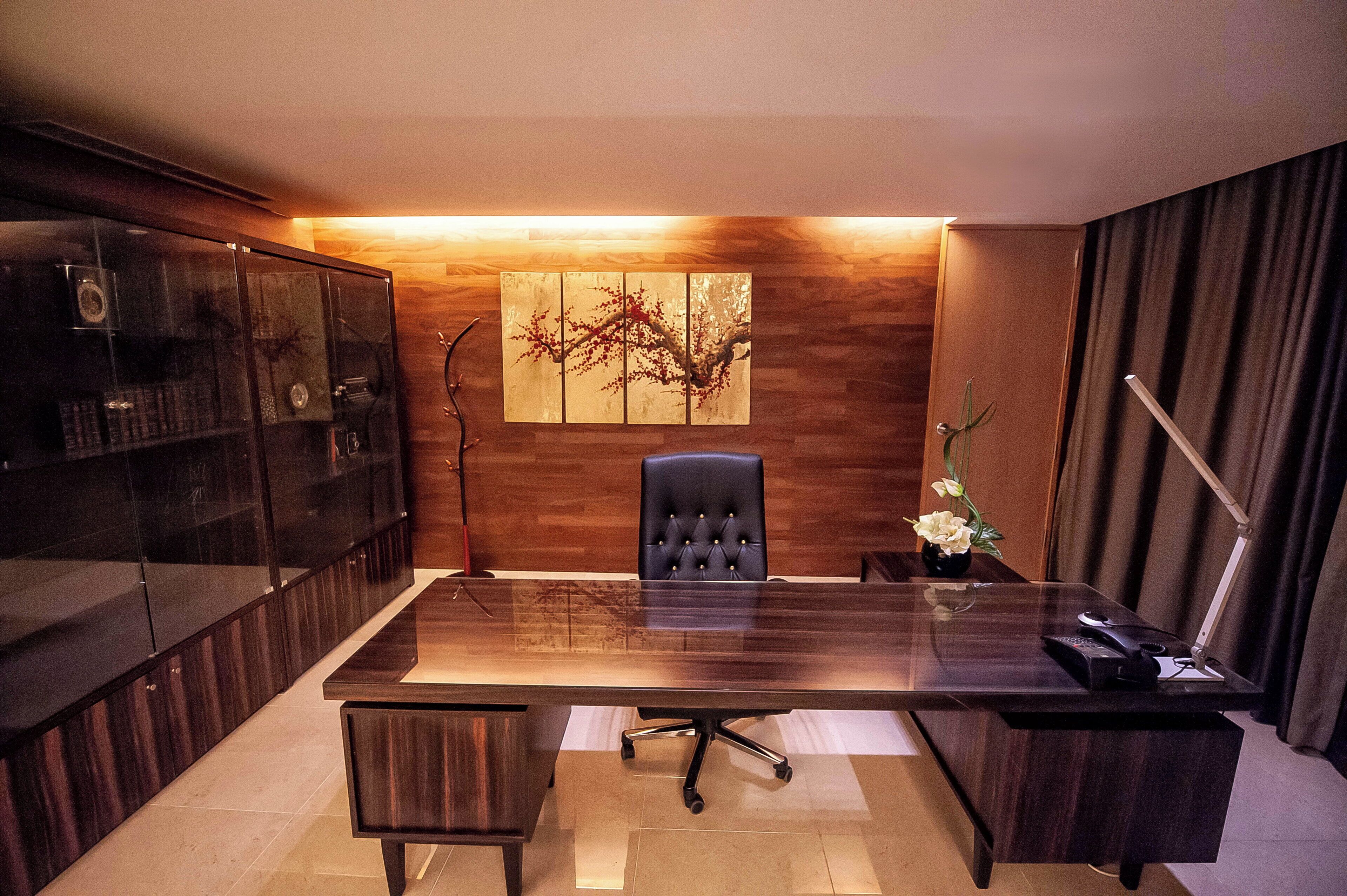 A modern office space with a long table, a black office chair, a cabinet with glass doors, and a wall-mounted artwork.