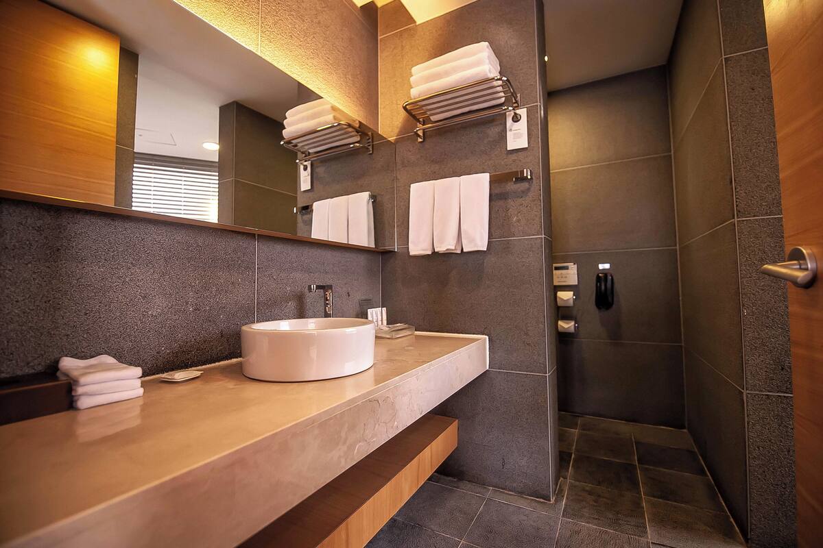 A modern bathroom with a large mirror, a round sink, and a walk-in shower.