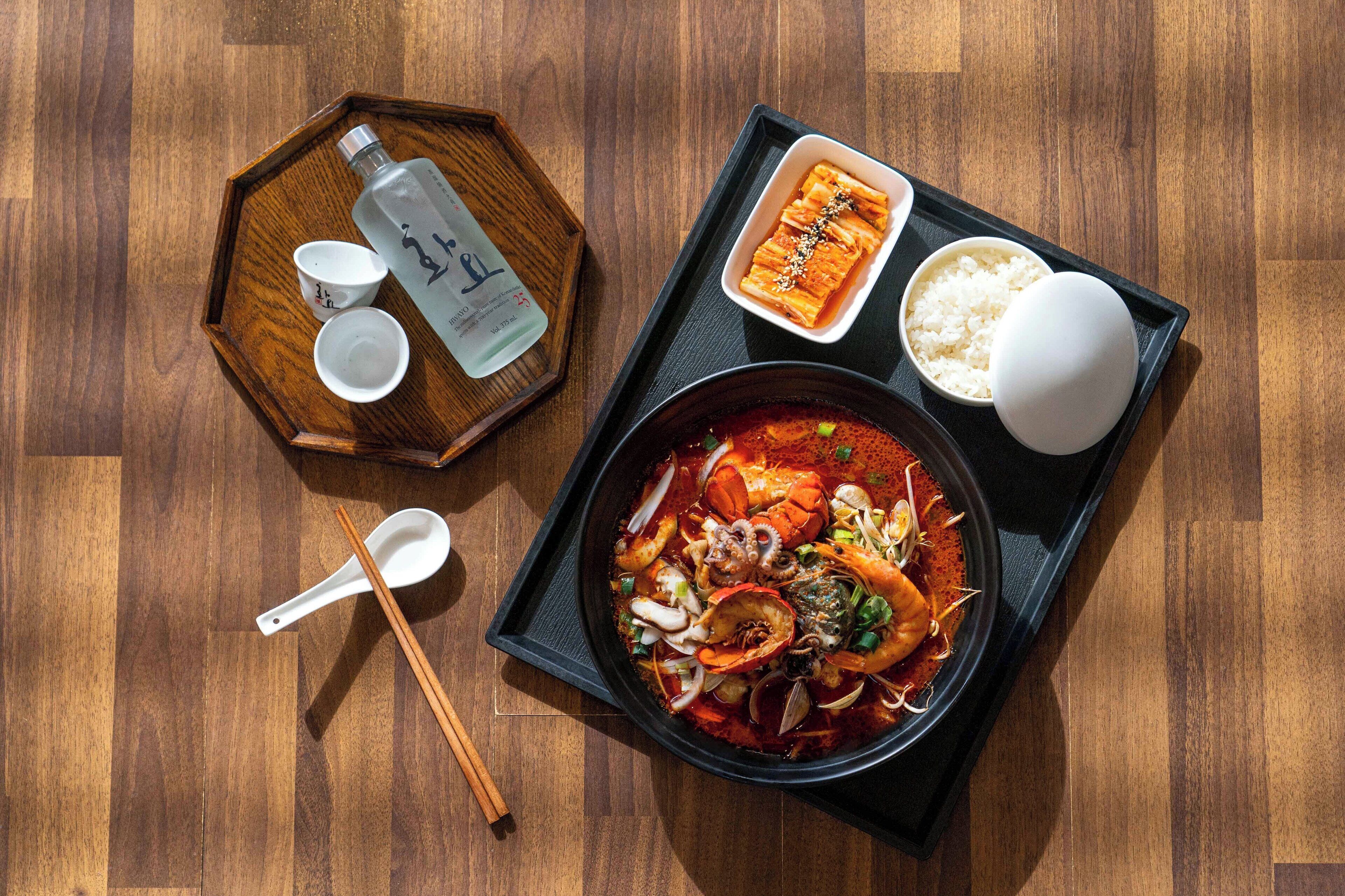 A tray with a seafood dish, rice, and a bottle of water on a wooden table.