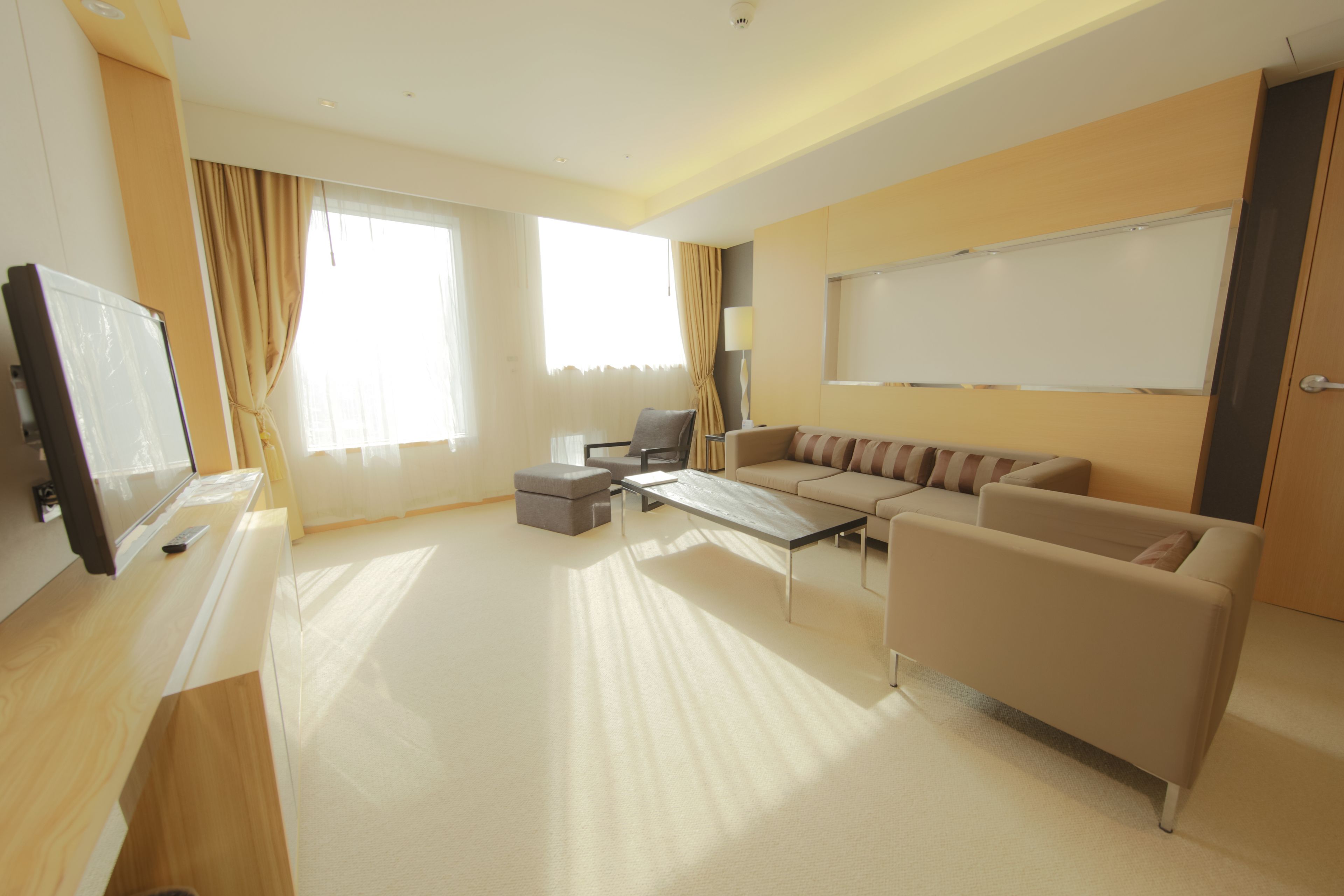A modern hotel room with a sofa, armchair, and a flat-screen TV.