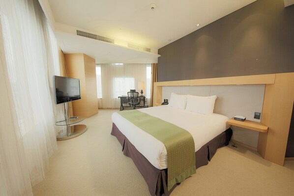 A hotel room with a large bed, a TV, a desk, and a chair.