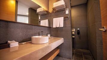 A modern bathroom with a large mirror, a round sink, and a walk-in shower.