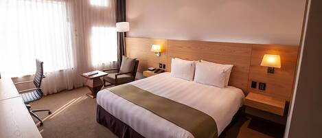 Habitación de hotel con una cama grande, dos lámparas de noche, un escritorio con silla y una ventana con cortinas.