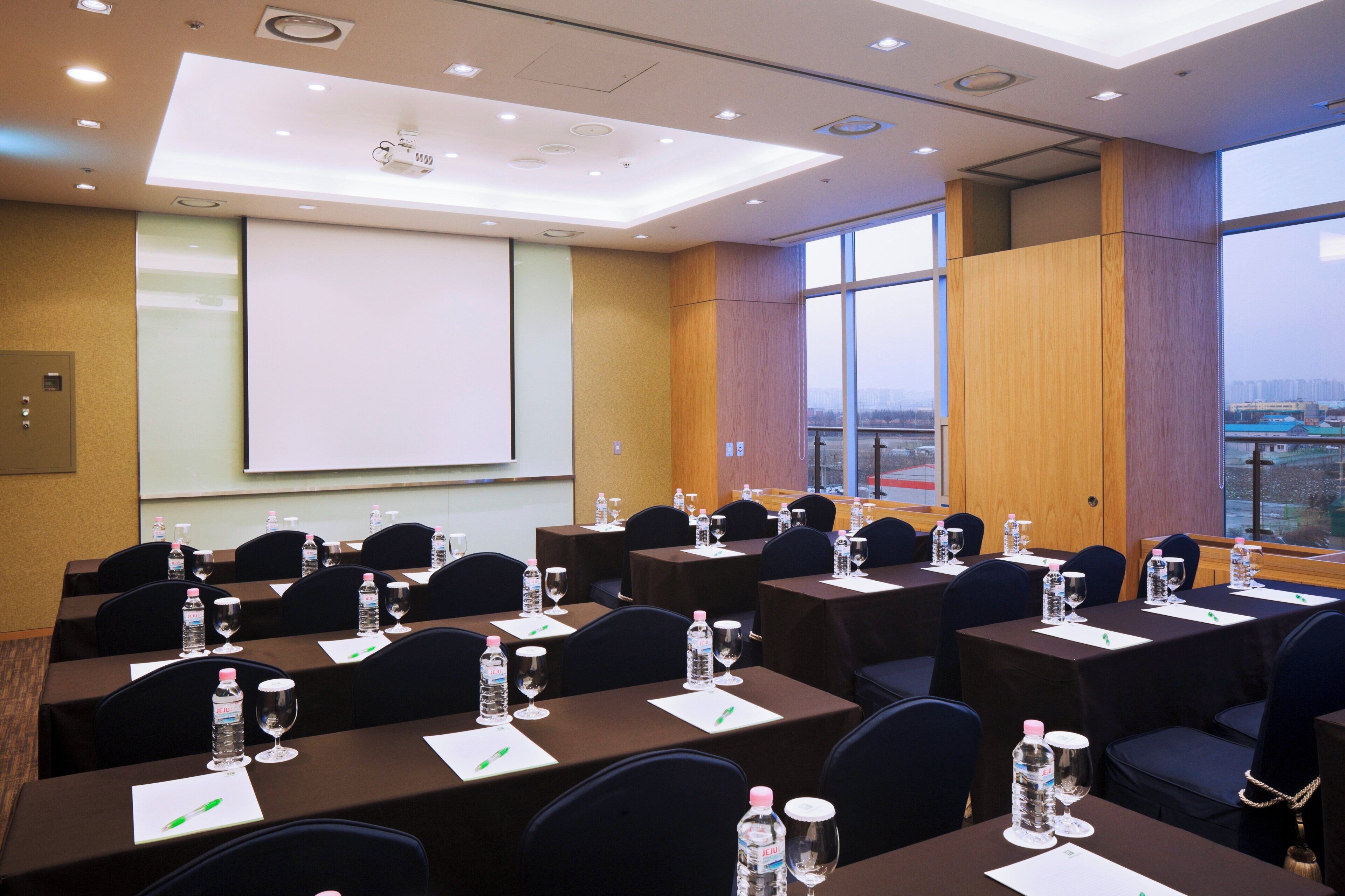 A conference room with tables set for meetings, equipped with water bottles and pens, and a projector screen.