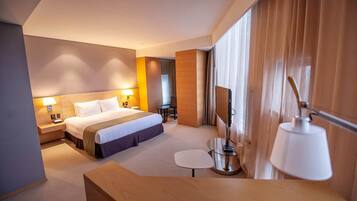 A hotel room with a large bed, bedside lamps, a TV, a small table, and a desk.