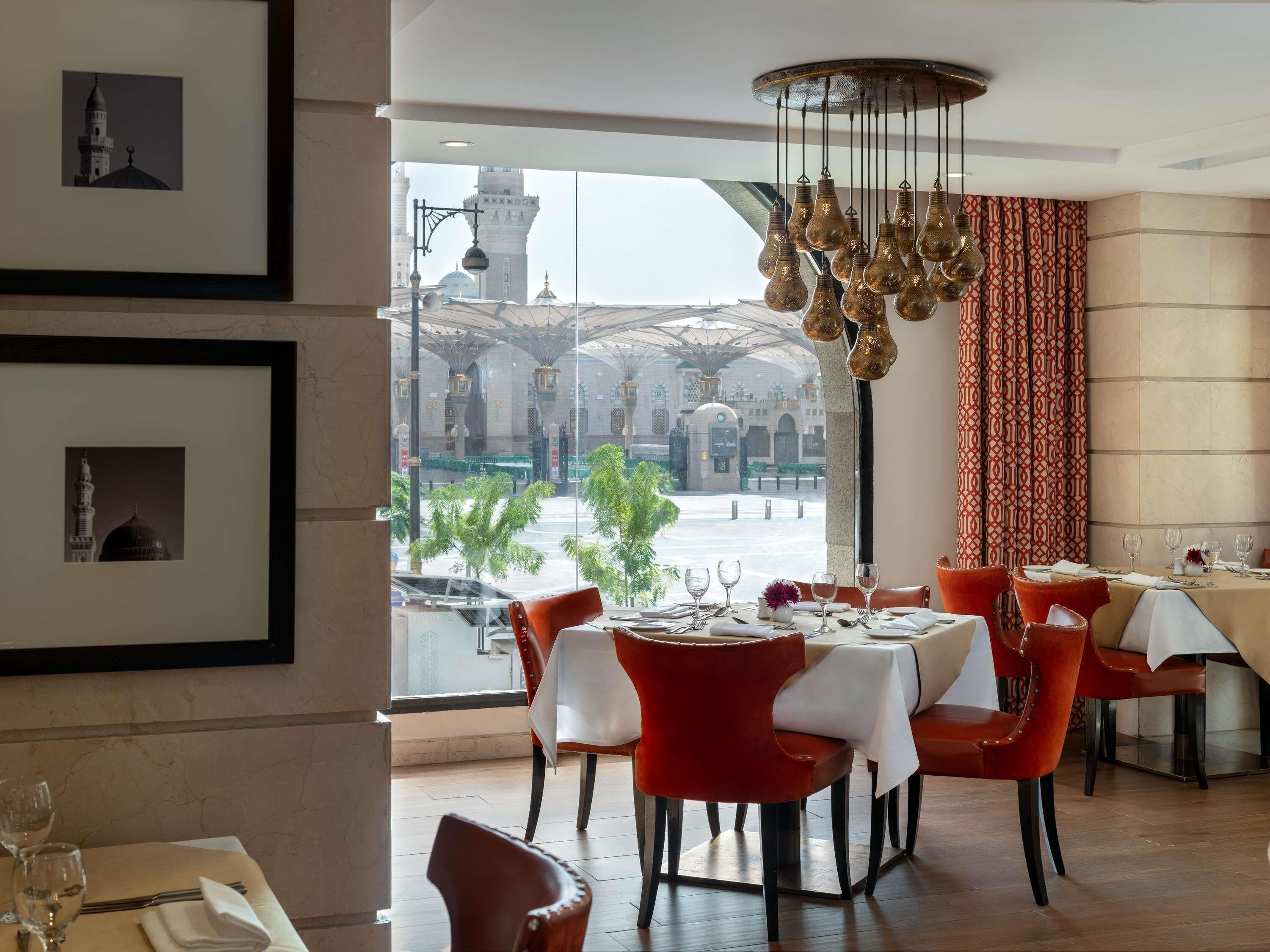 Un restaurante con vistas a una mezquita, sillas rojas y un candelabro.