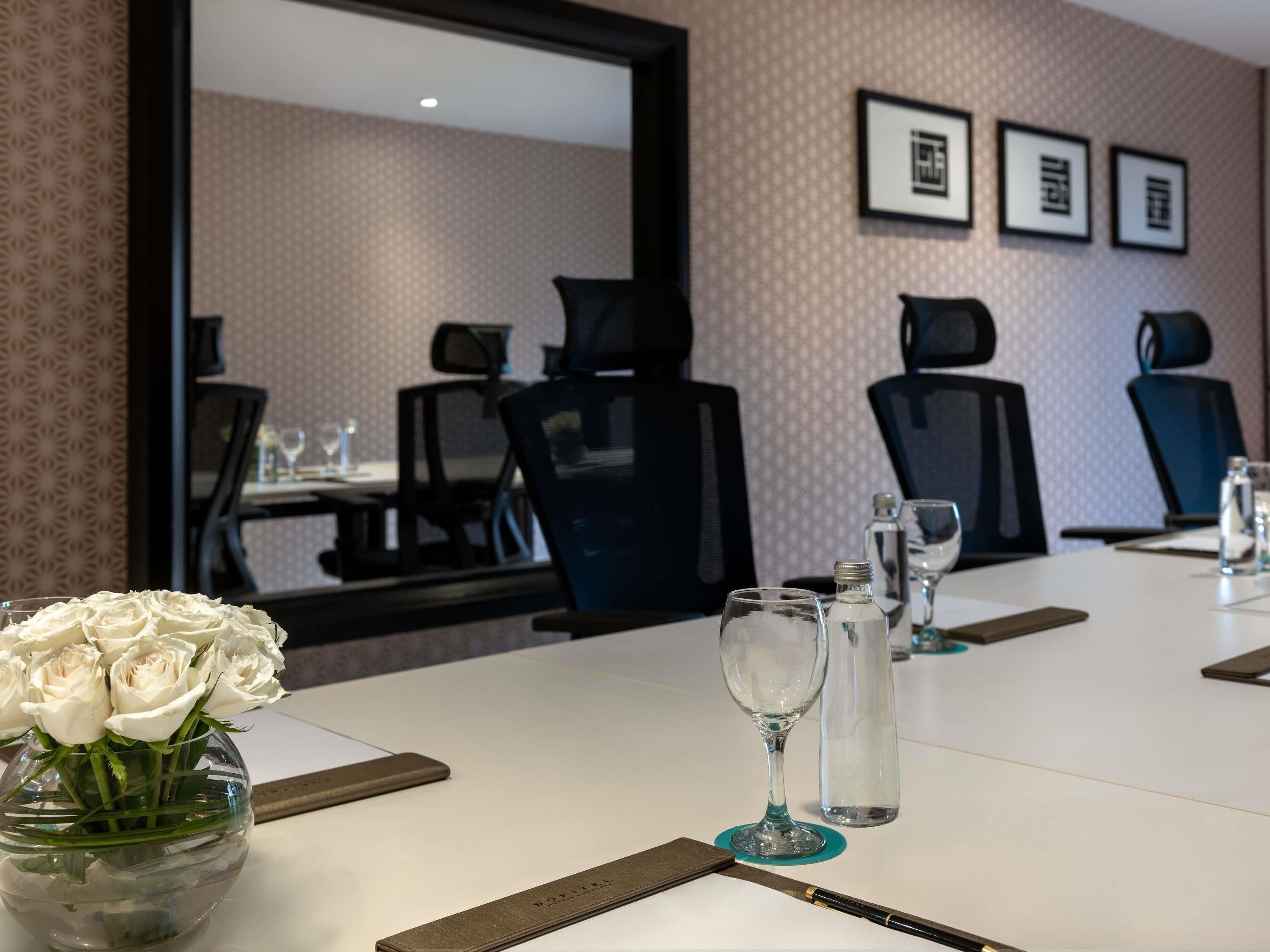 A conference room with a white table, chairs, a vase of white roses, and framed pictures on the wall.