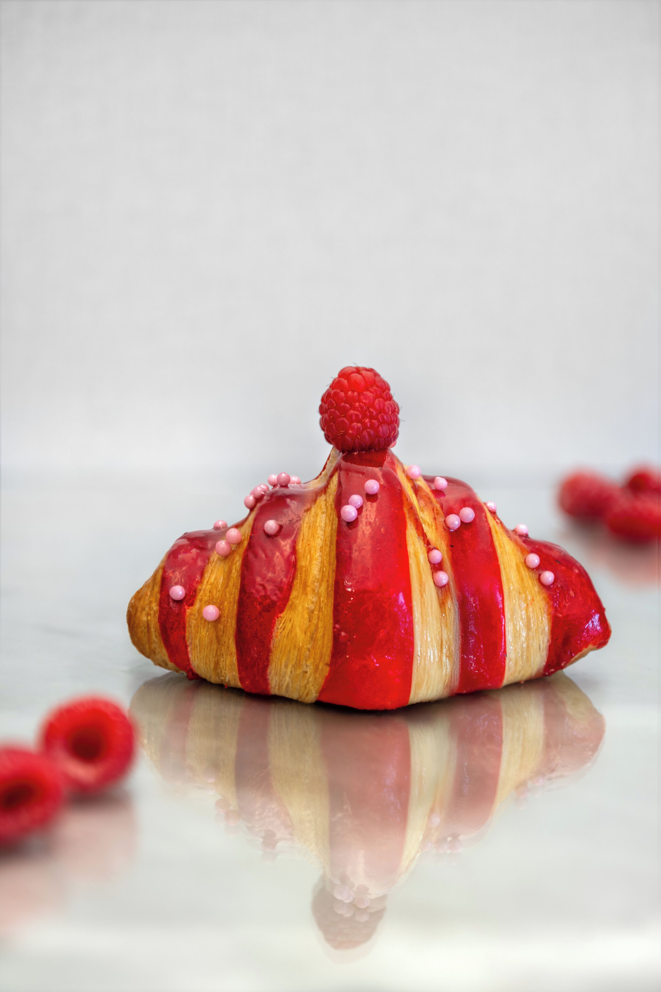 A dessert with a raspberry on top, surrounded by small pink dots.
