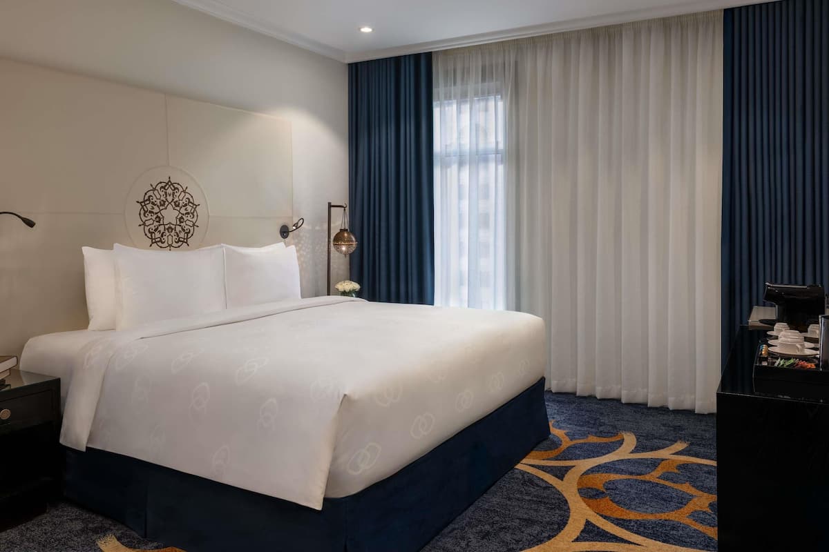 Een hotelkamer met een groot bed, een nachtkastje, een wandlamp en een raam met gordijnen.