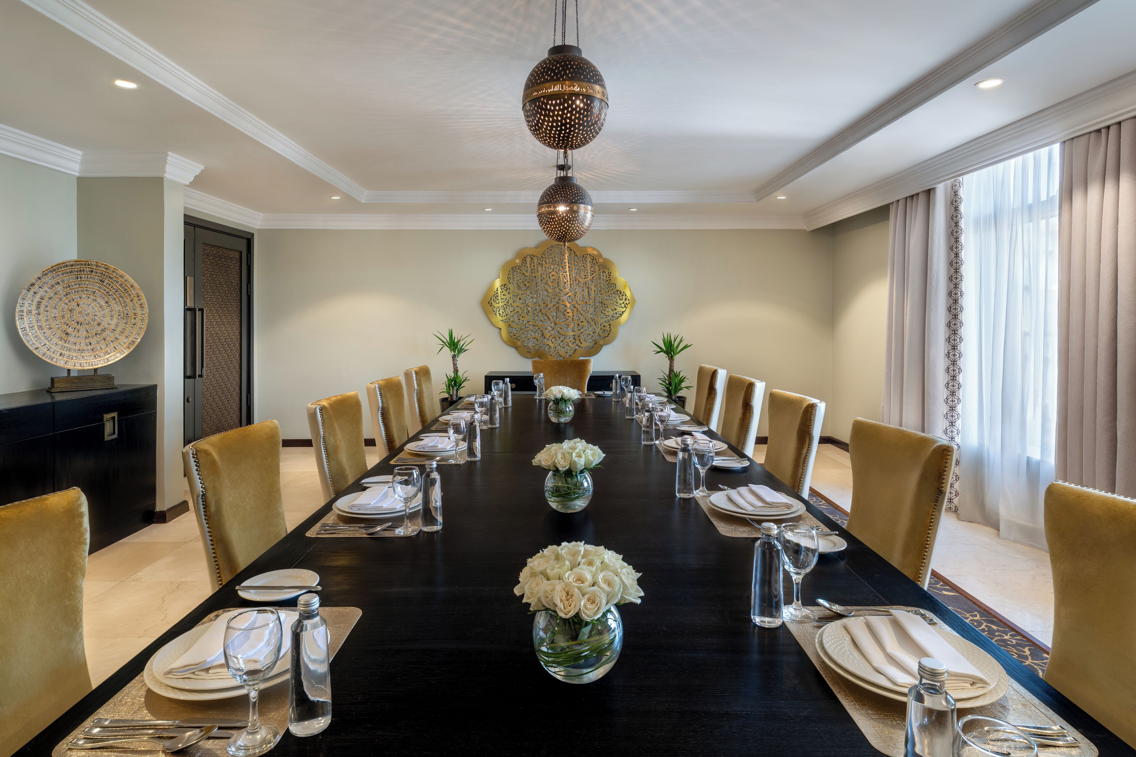 A long dining table set for a formal meal with chairs, a decorative centerpiece, and a chandelier.