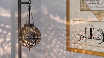 A framed Arabic calligraphy on a wall, a hanging lantern, and a vase with white flowers on a table.