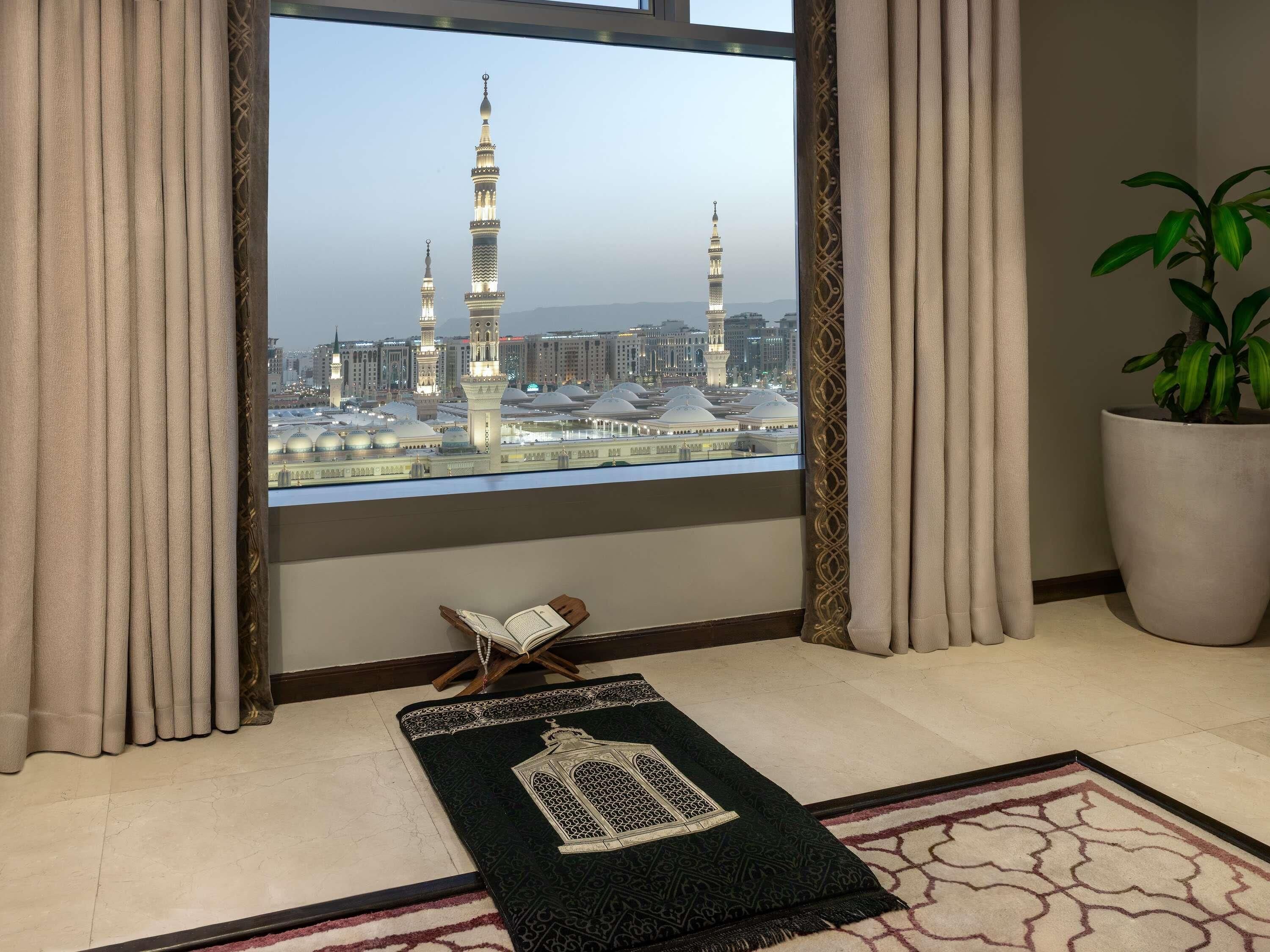 Une pièce avec vue sur une mosquée, un tapis de prière et une plante en pot.