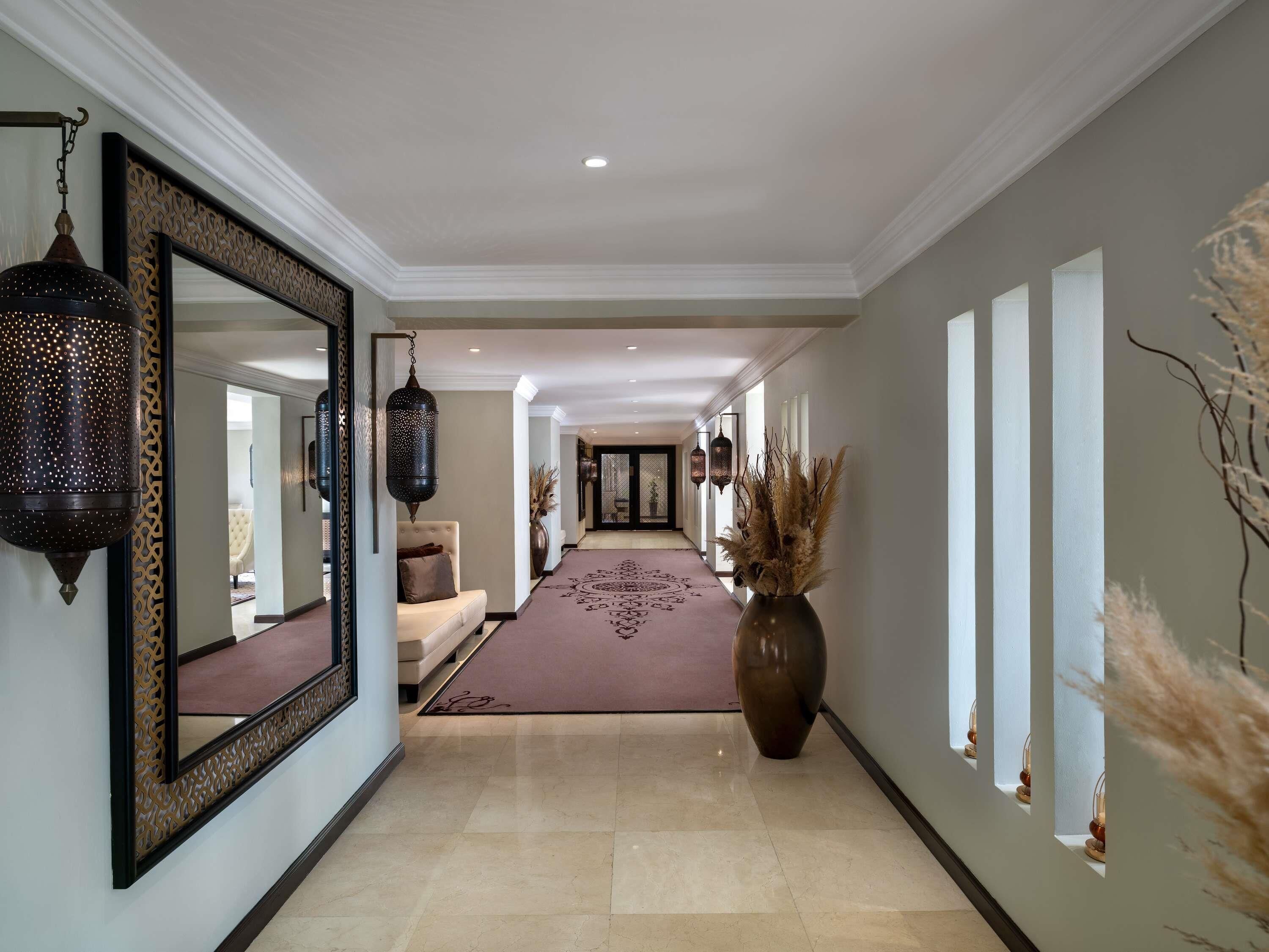 A hallway with a large mirror, hanging lanterns, a decorative vase, and a patterned carpet.