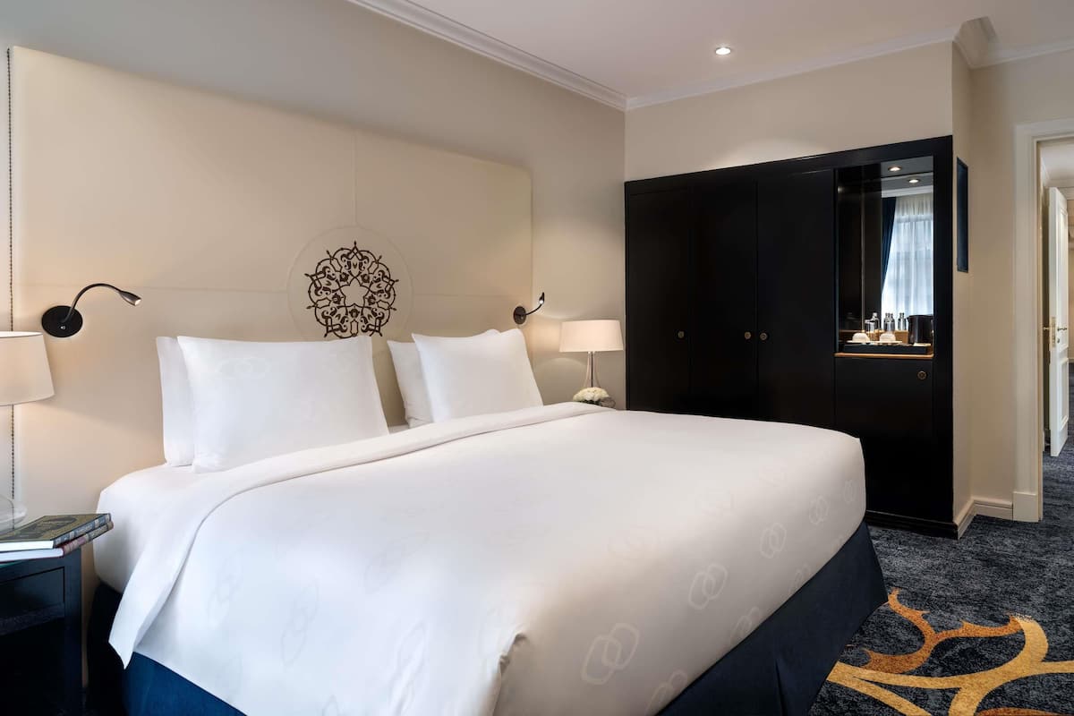 Een hotelkamer met een groot bed, twee bedlampen, een decoratief wandobject, een kledingkast en een spiegel.