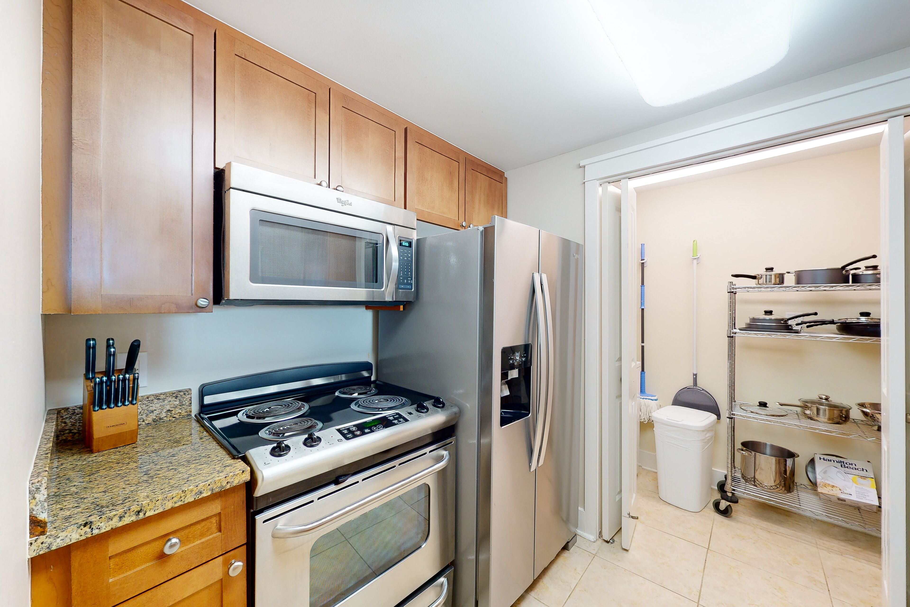 A kitchen with a stove, microwave, refrigerator, wooden cabinets, and a pantry with pots and pans.