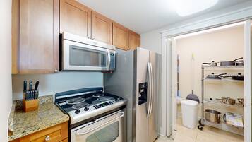 A kitchen with a stove, microwave, refrigerator, wooden cabinets, and a pantry with pots and pans.