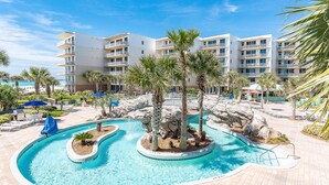A resort with a pool area featuring palm trees, a rock formation, and a view of the ocean. - Waterscape Condominiums (Fort Walton Beach)