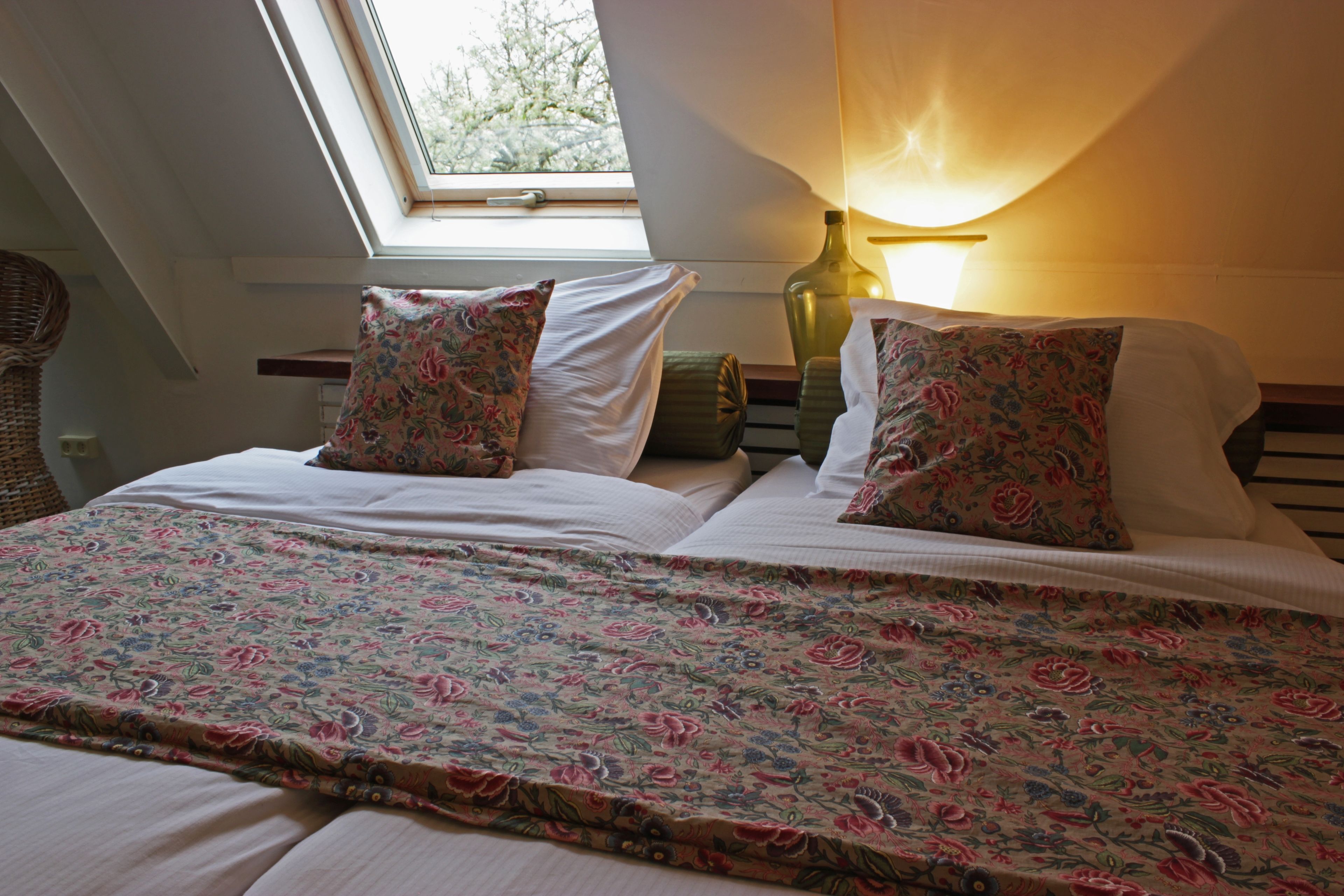 Un dormitorio con tragaluces, ropa de cama estampada con flores y una lámpara de noche.