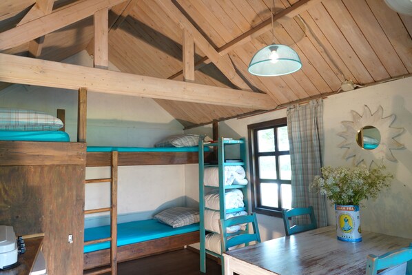 A rustic room with bunk beds, a wooden table, and a window with curtains. - B&B en camping Welgelegen (Workum)