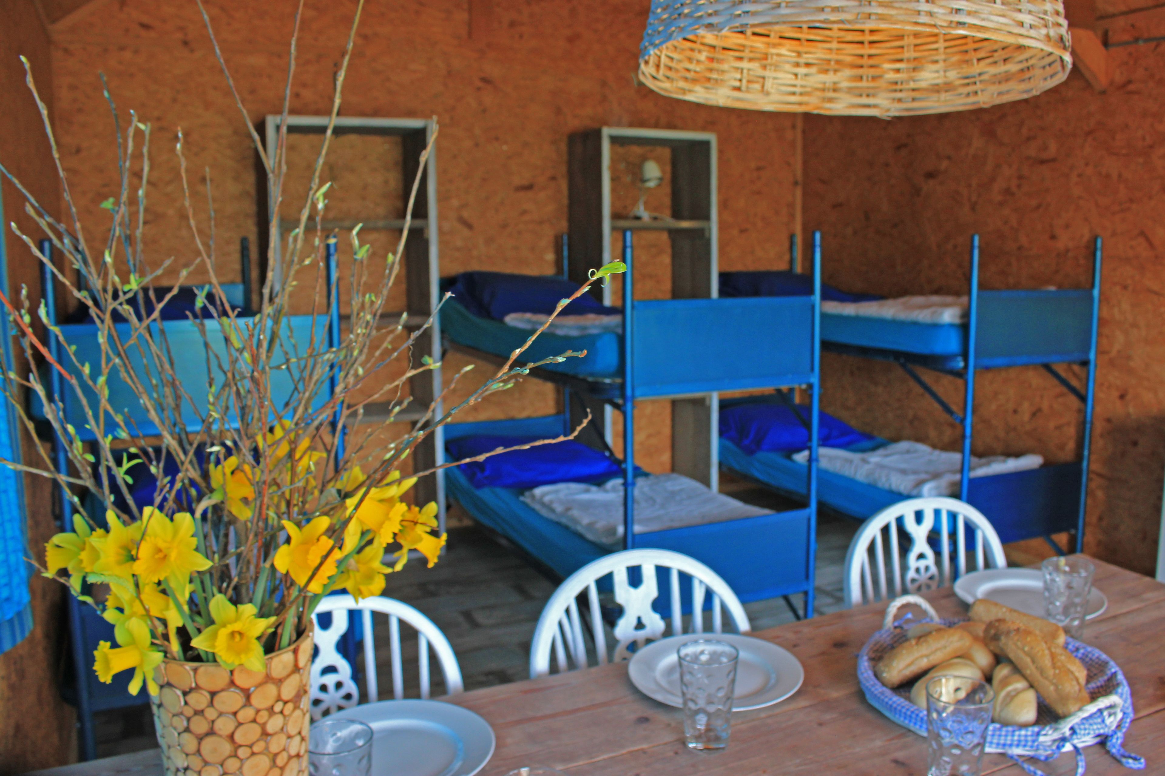 A rustic room with bunk beds, a dining table with chairs, and a basket of bread.