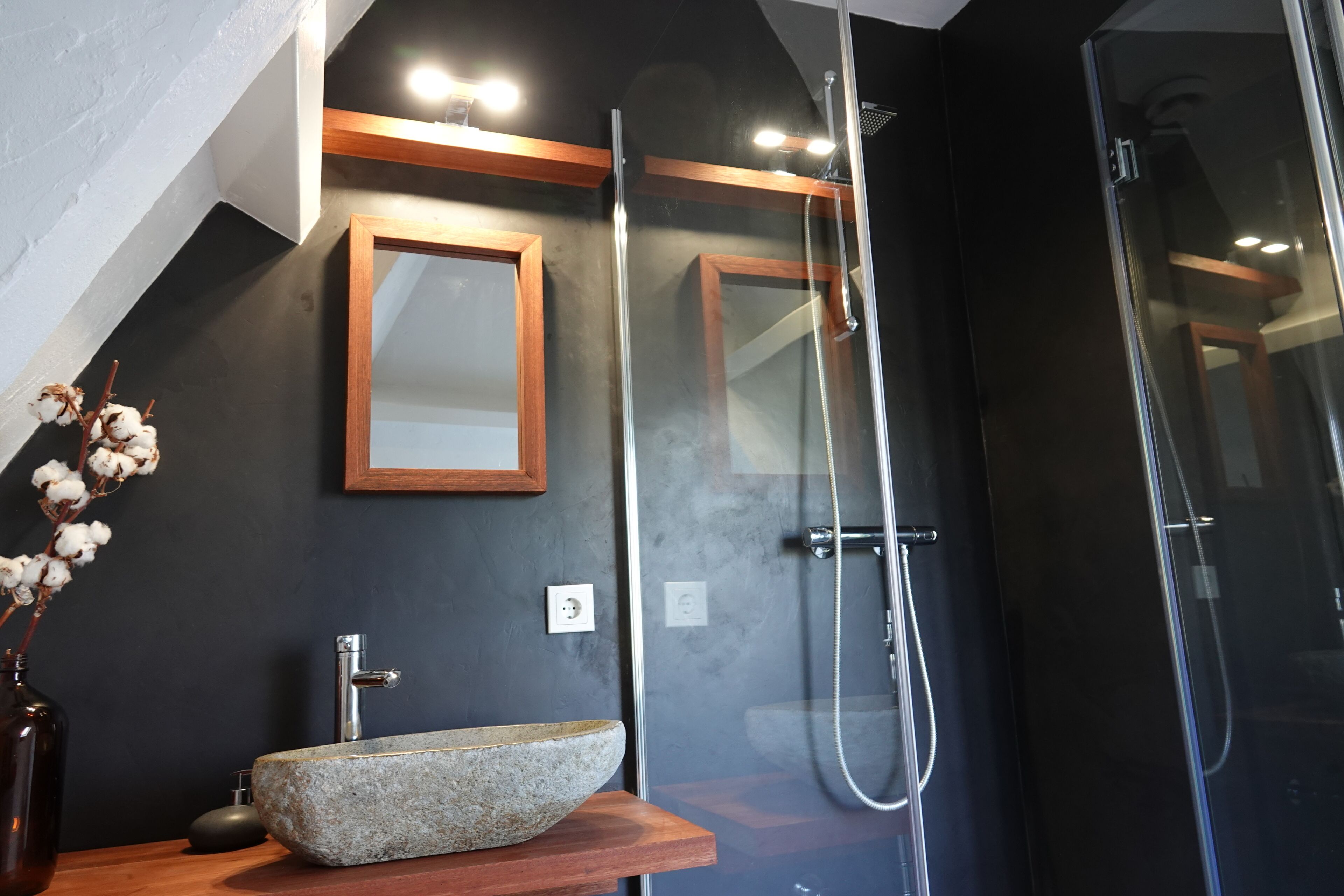 Un bagno moderno con lavabo in pietra, piano in legno e cabina doccia in vetro.
