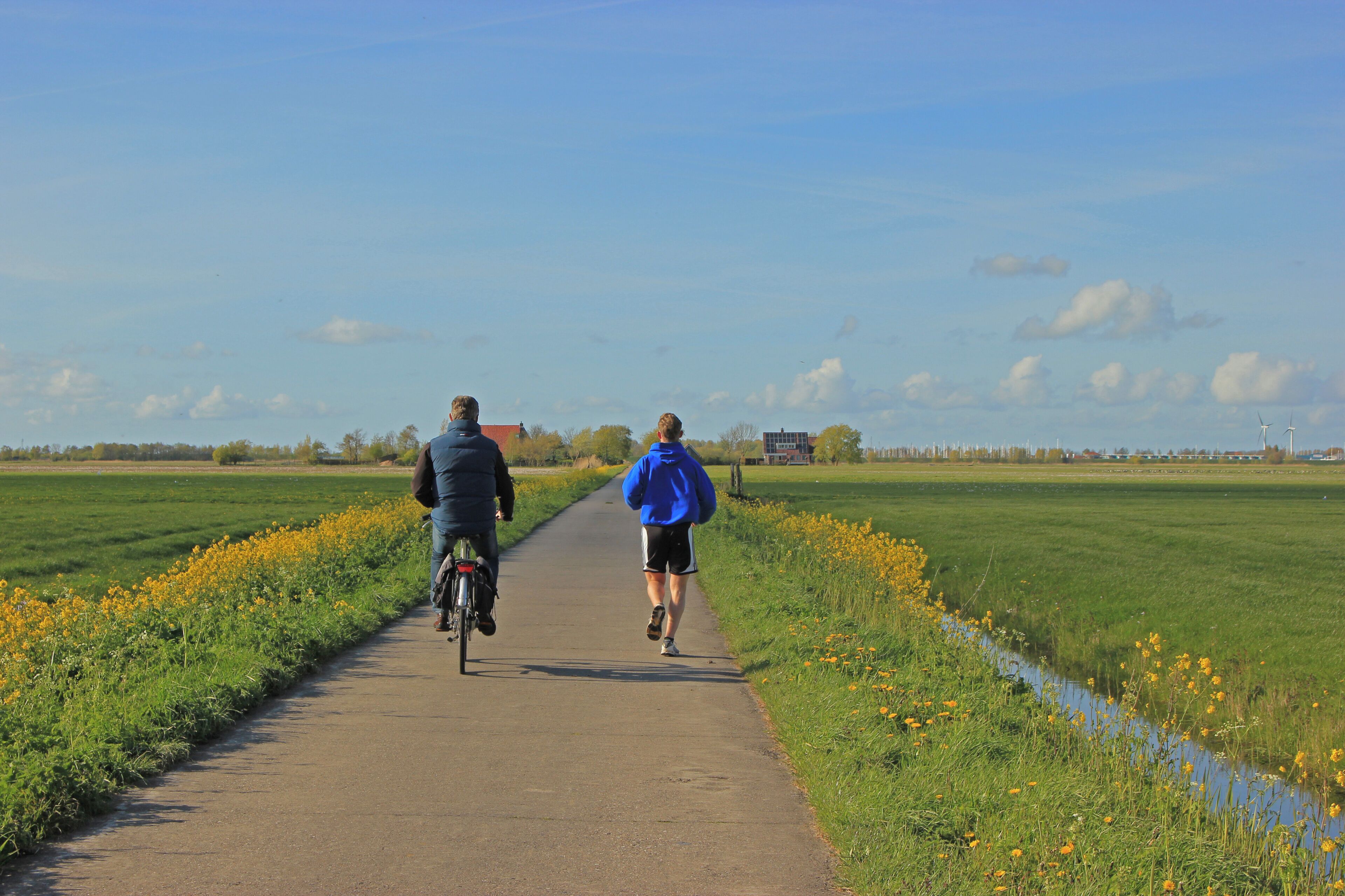 A pathway flanked by fields and a small water channel, with two individuals cycling and walking.