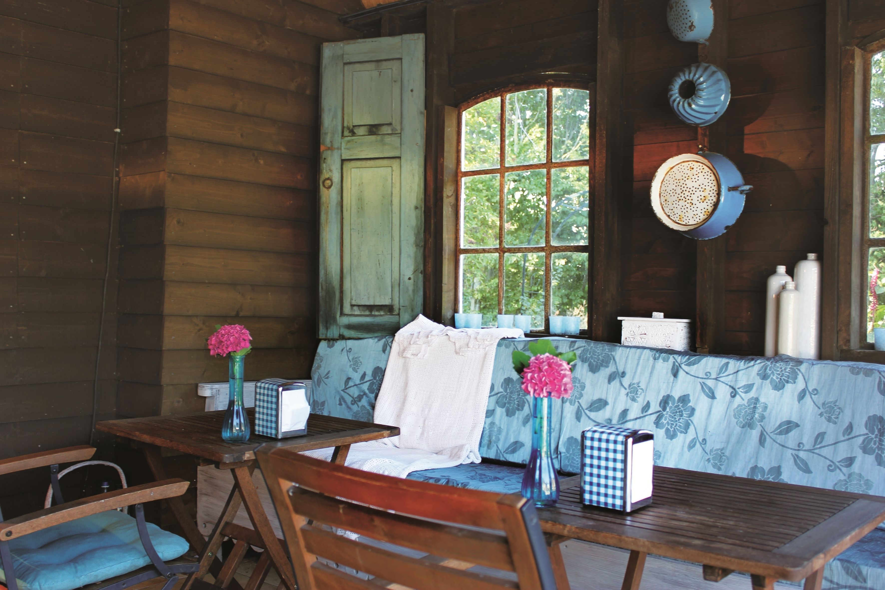 Interior de una cabaña de madera con comedor, un banco y una ventana con vistas a árboles.